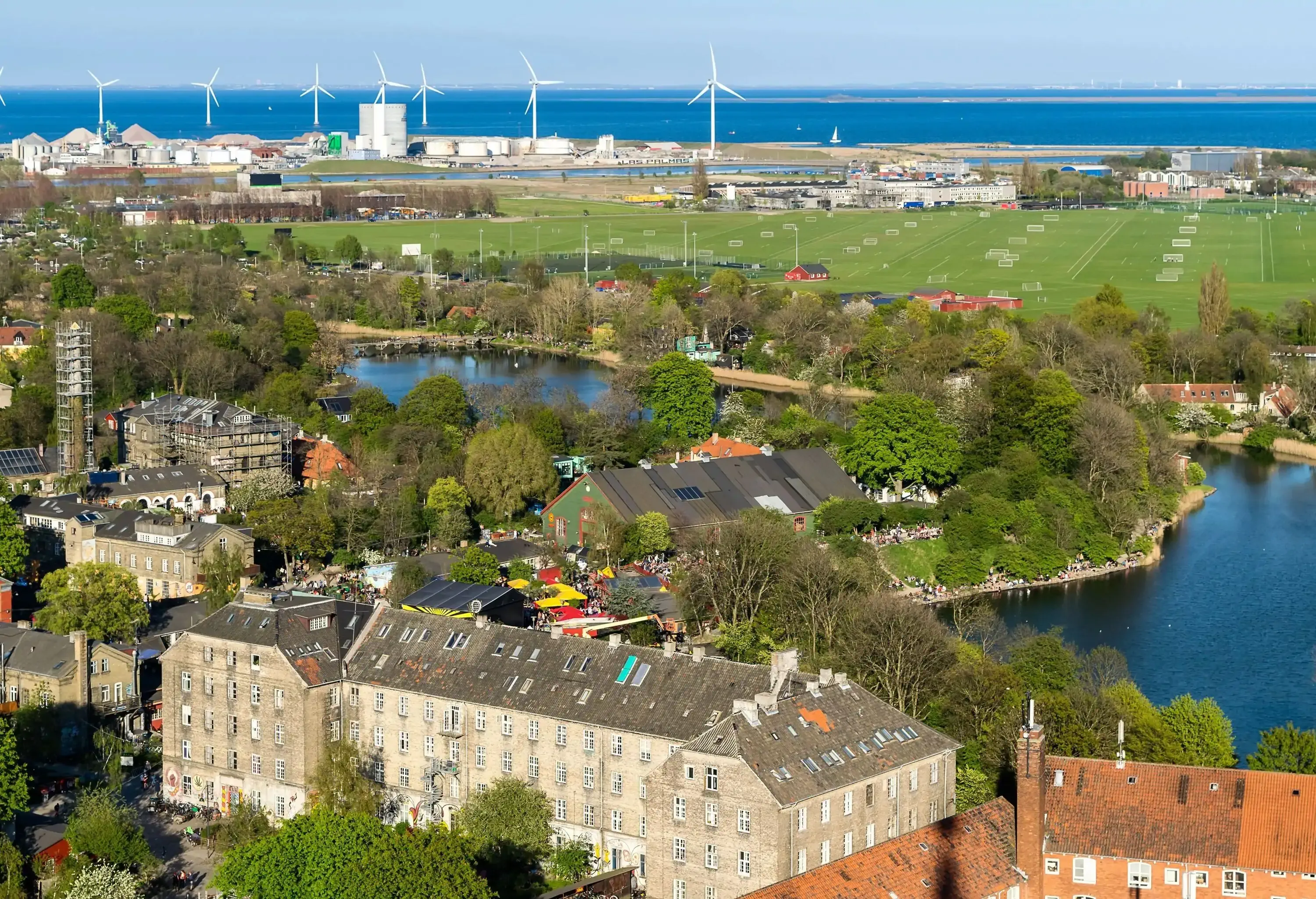 A populous neighbourhood surrounding a body of water, with wind turbines in the background.