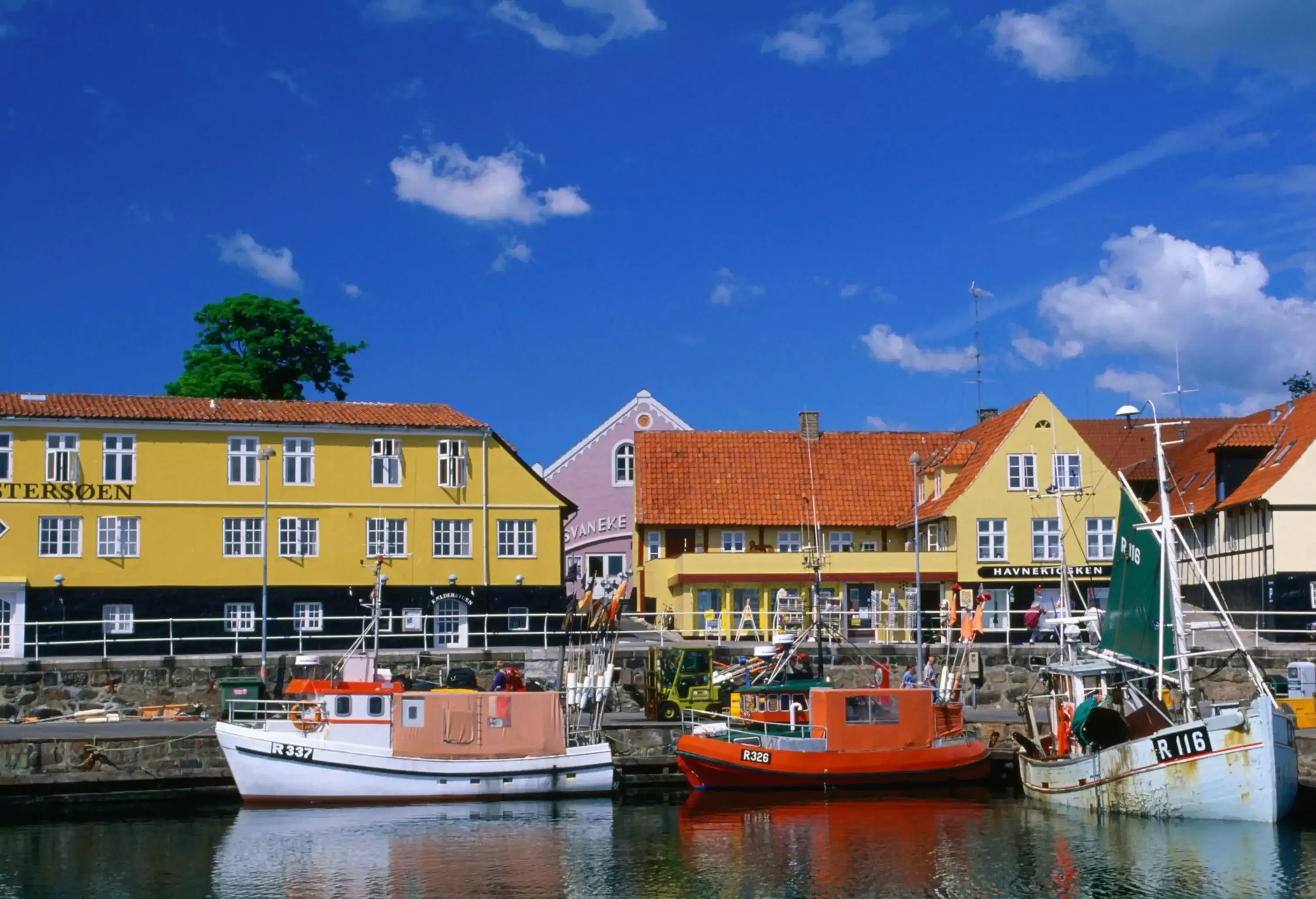 Fishing boats docked in a harbour across colourful buildings on the coast.