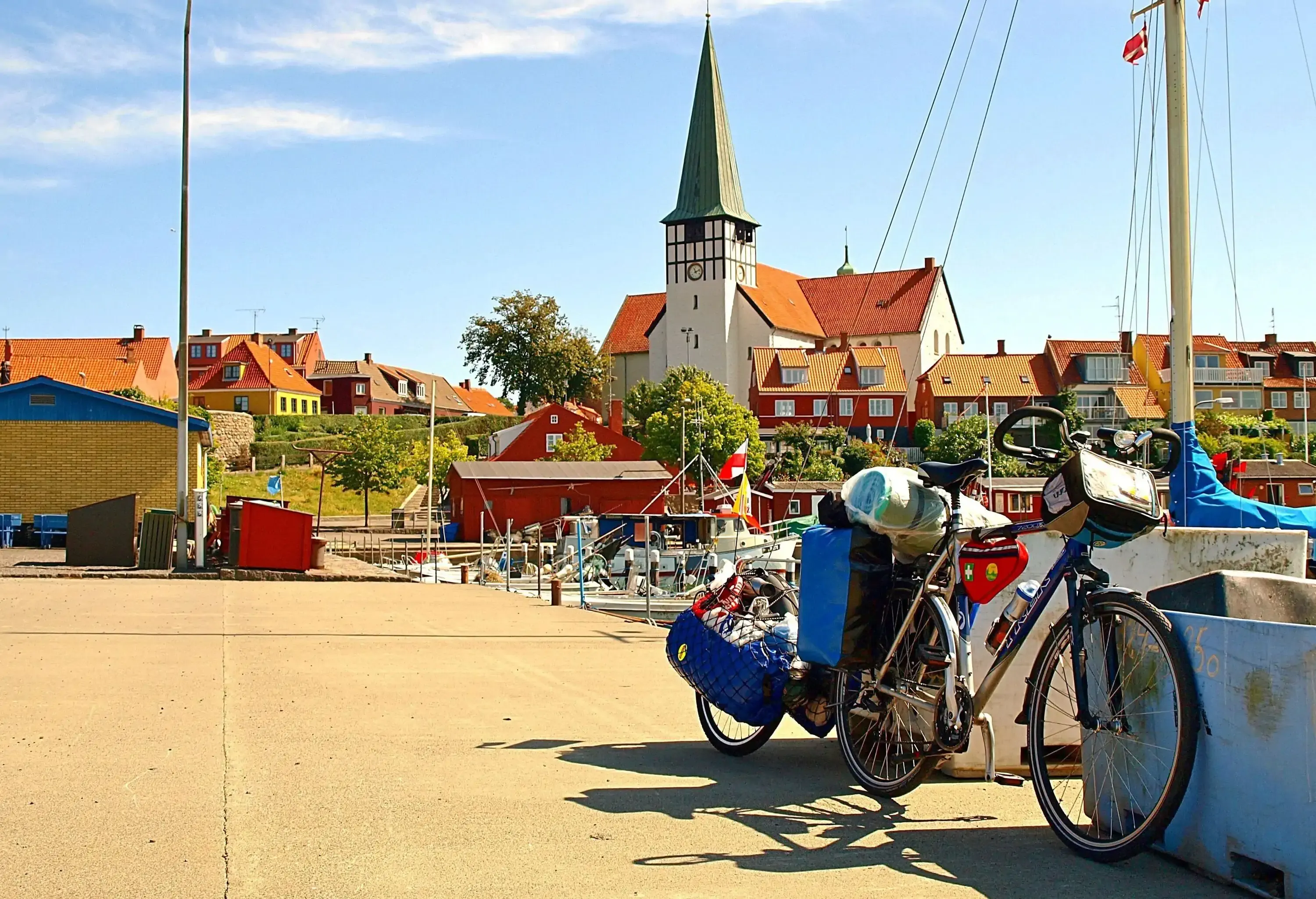 A bicycle parked on a harbour with views of a clock tower that rises above a townscape. 