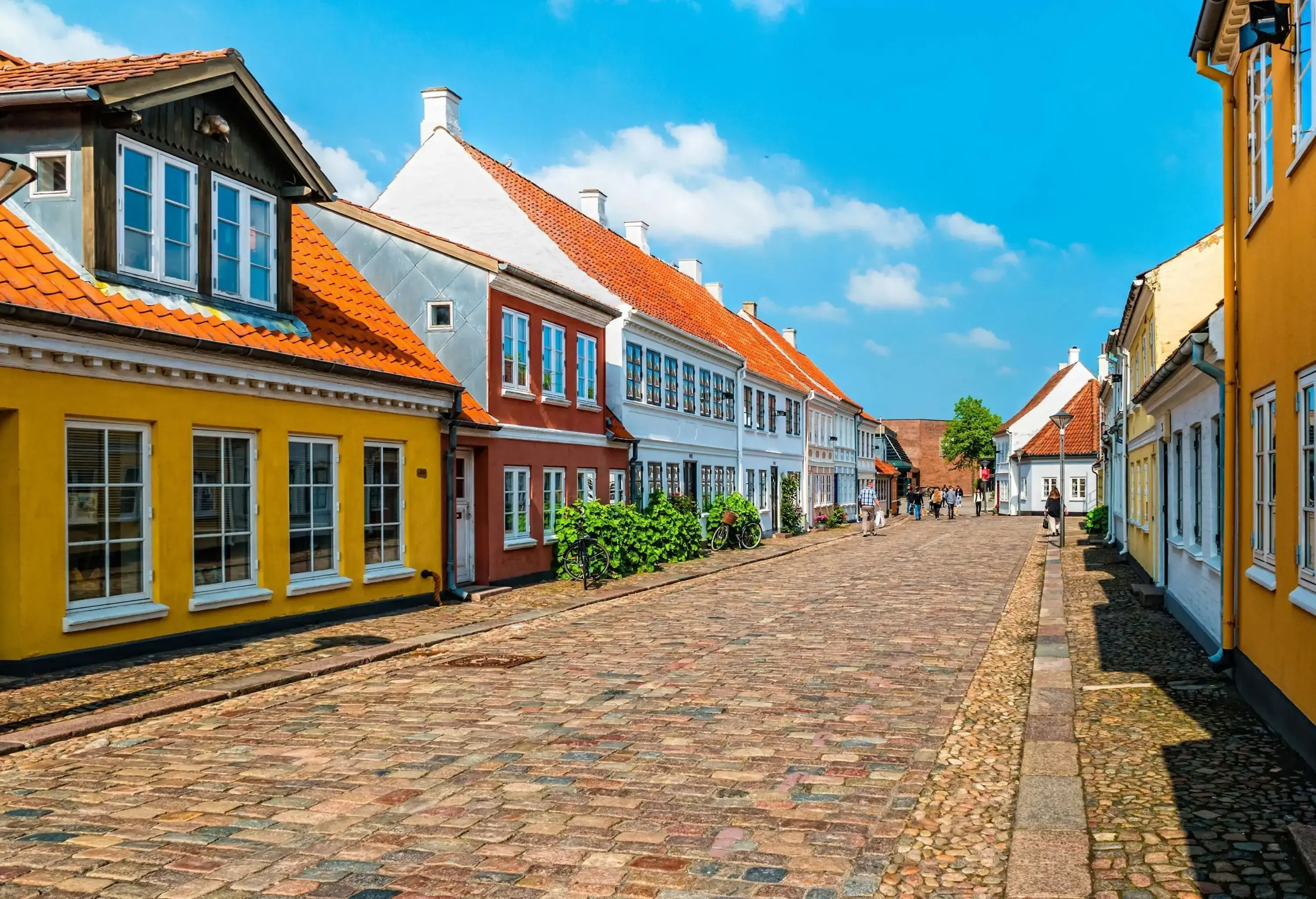 A cobblestone street bordered with colourful and vibrant concrete homes with glass windows and tiled roofs.