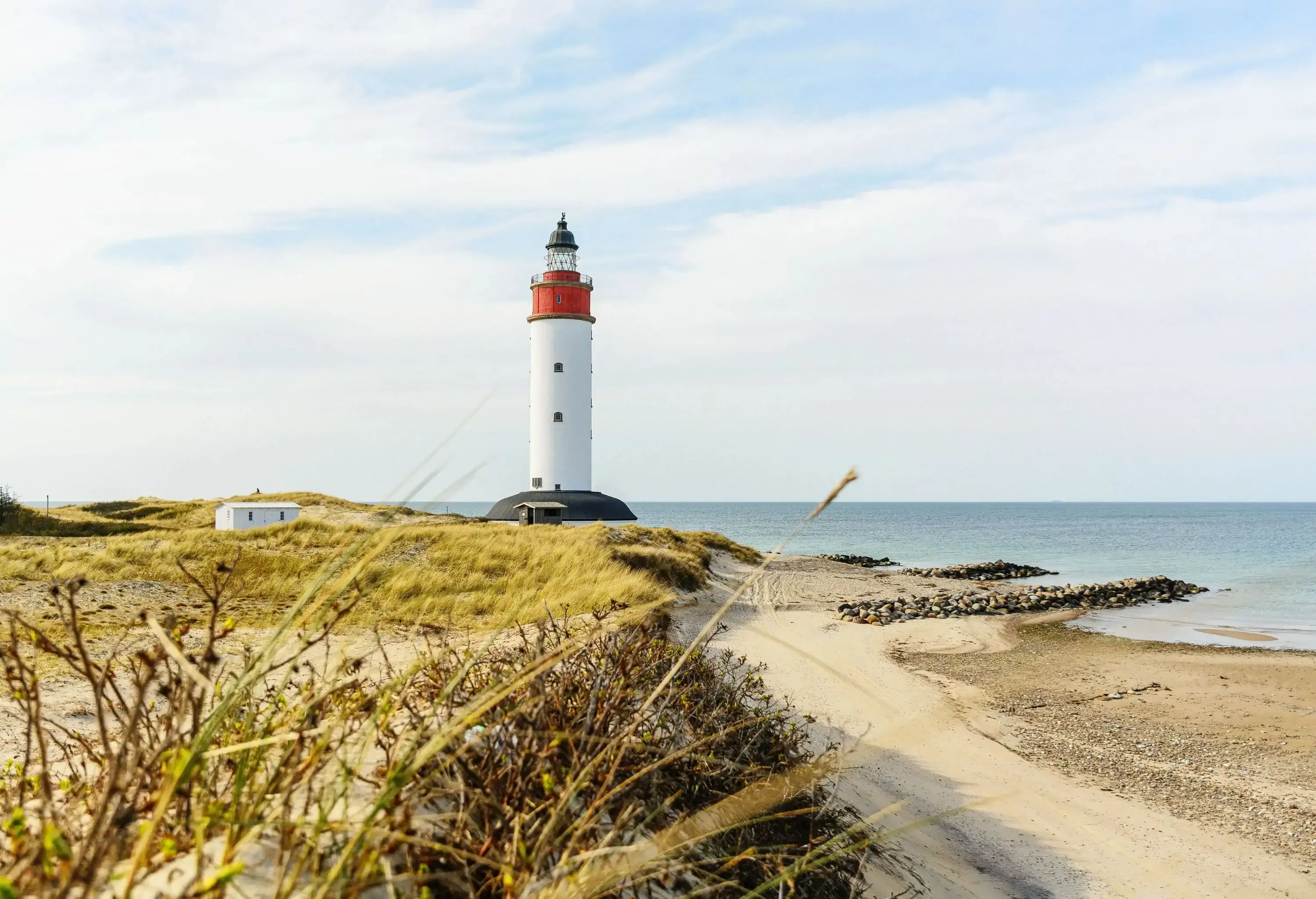 A lighthouse by sand dunes and beach on an overcast crisp day