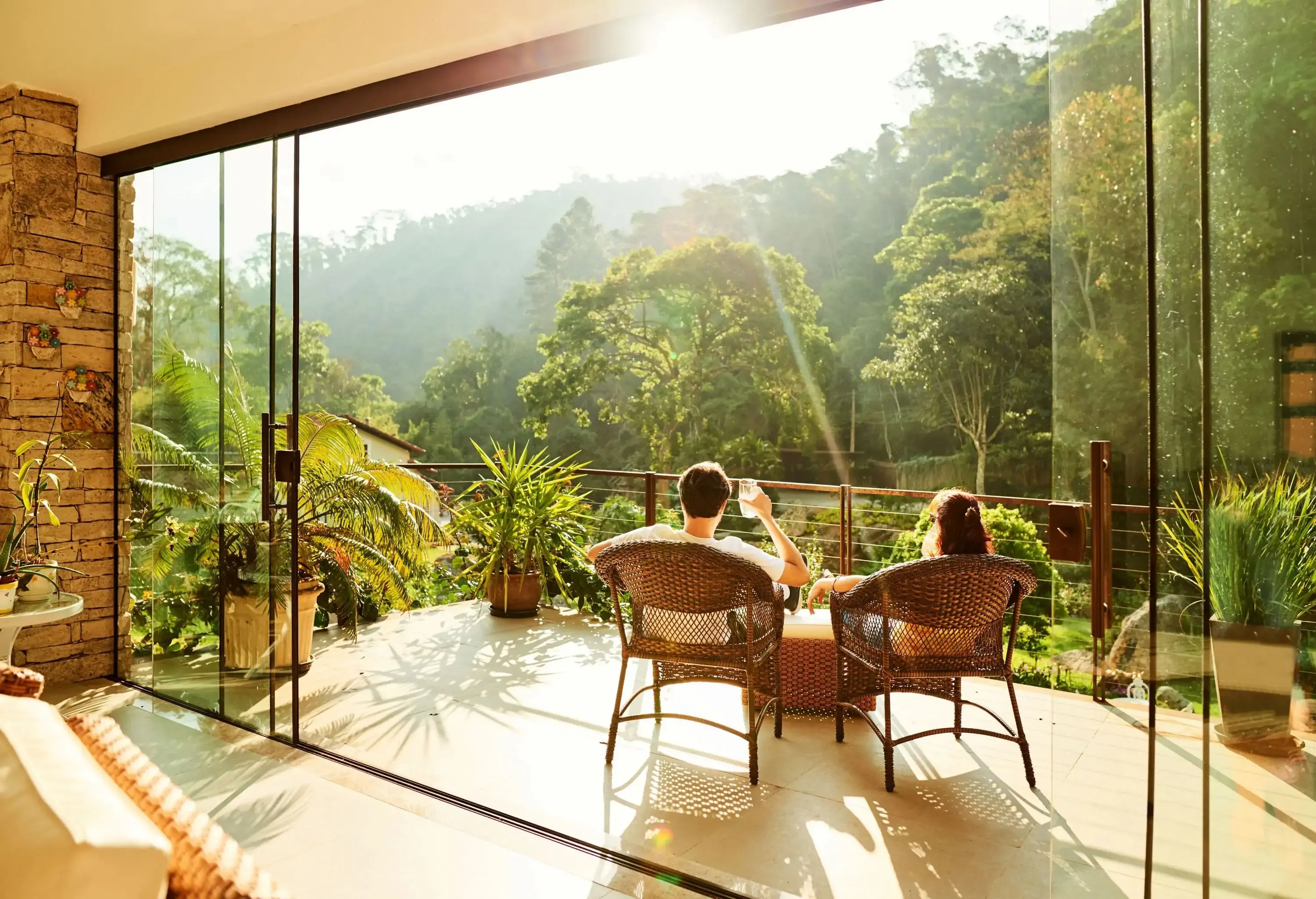 Two people sitting on wicker chairs on a terrace under the light of day.