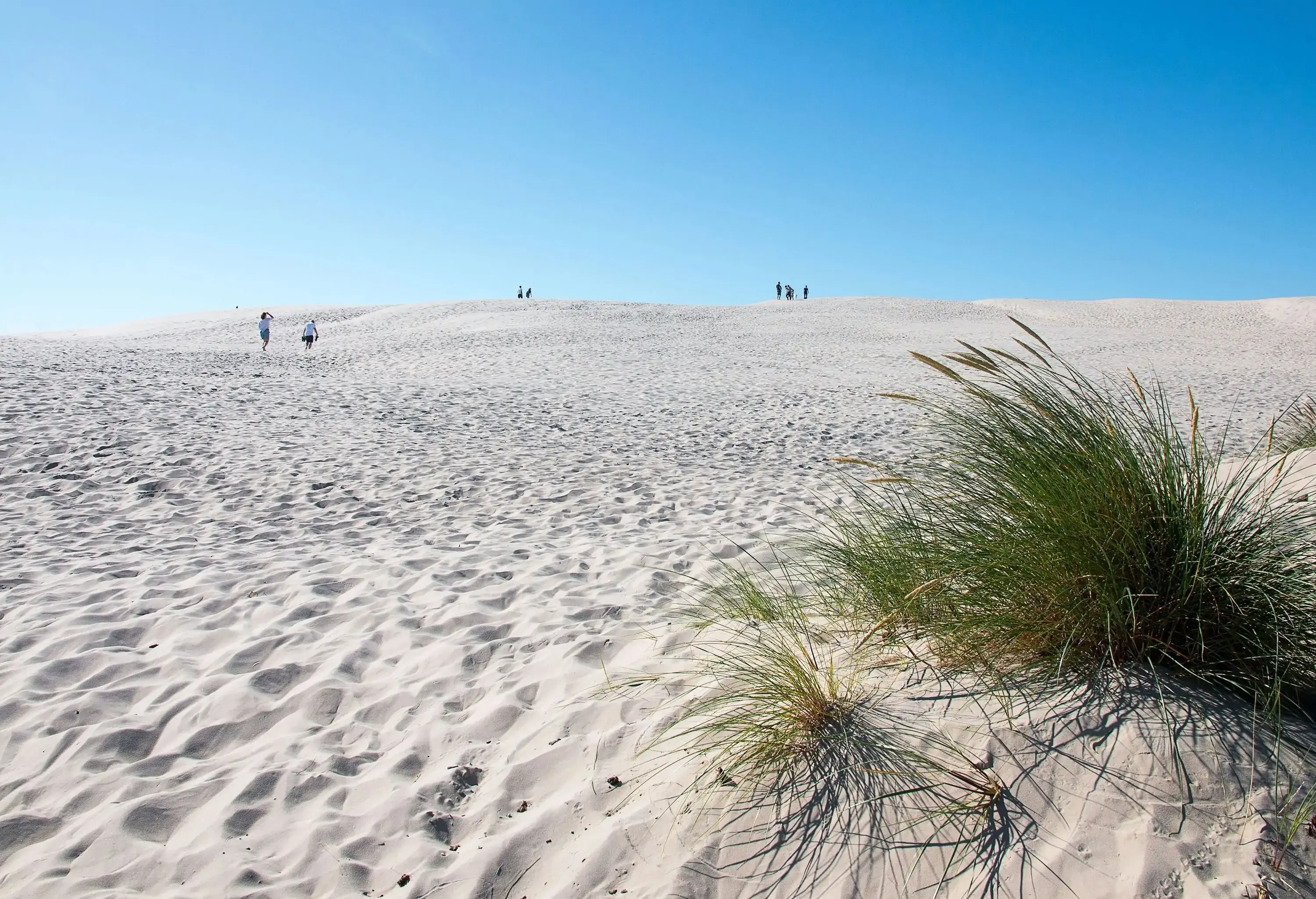 People stroll across a wide white sand beach.