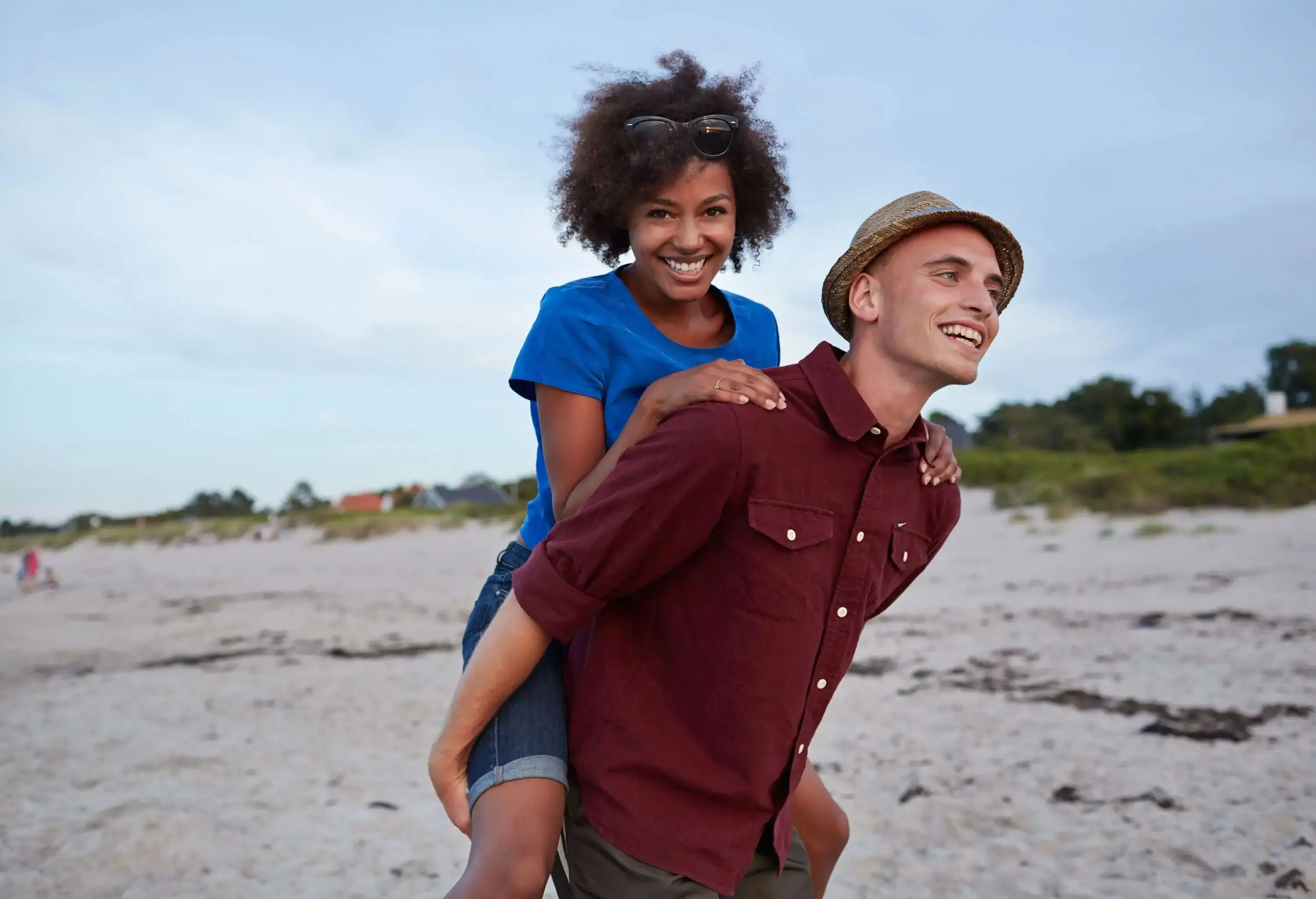 A man carries her girlfriend on his back along the beach.