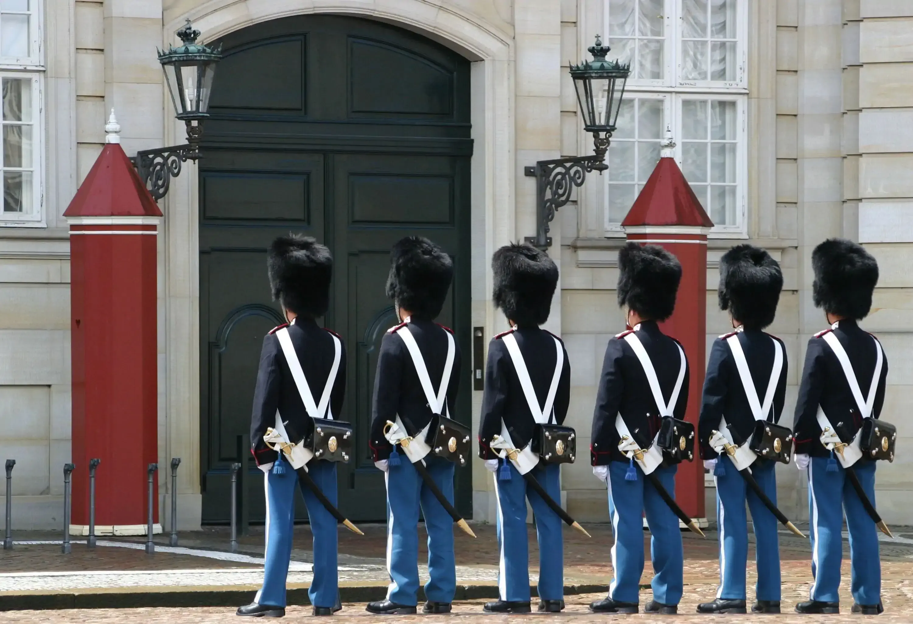 Royal guards standing in line in front of an entry doorway flanked by red sentry boxes.