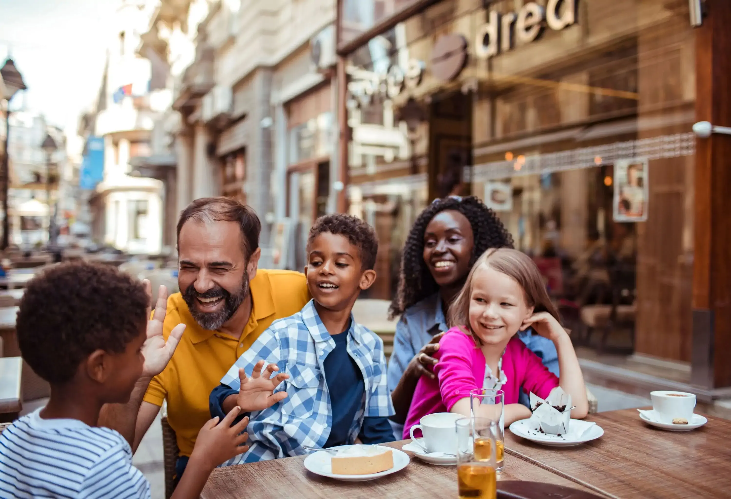 A couple and three kids chatting and laughing at a table in an outside restaurant.