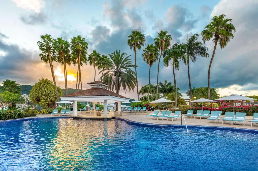 Sunset view of a tranquil large resort swimming pool with deckchairs and palm trees