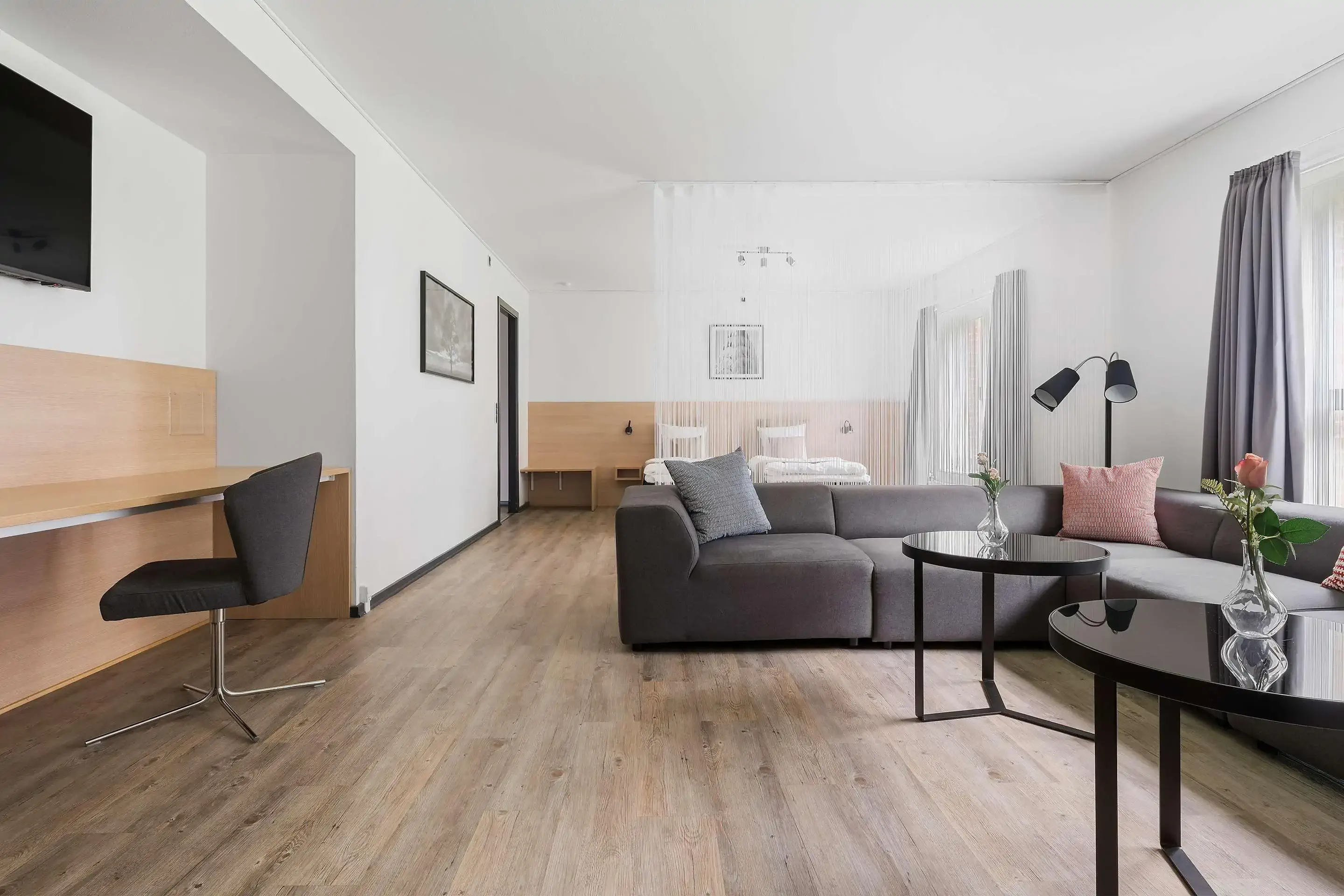 Modern nordic hotel suite with sofa and bed separated by a white string curtain