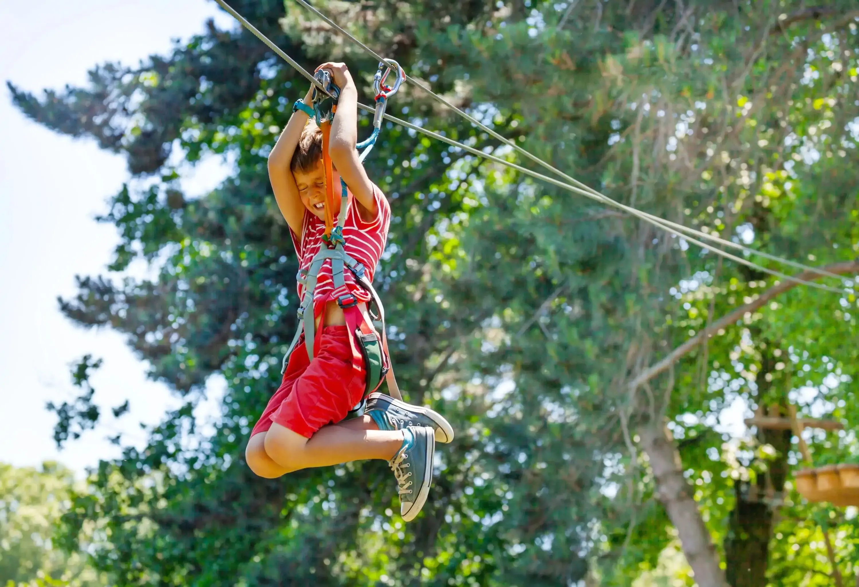 A boy slides down a fast zip line with a trolley, his eyes closed in pure excitement and thrill as he speeds along the line.