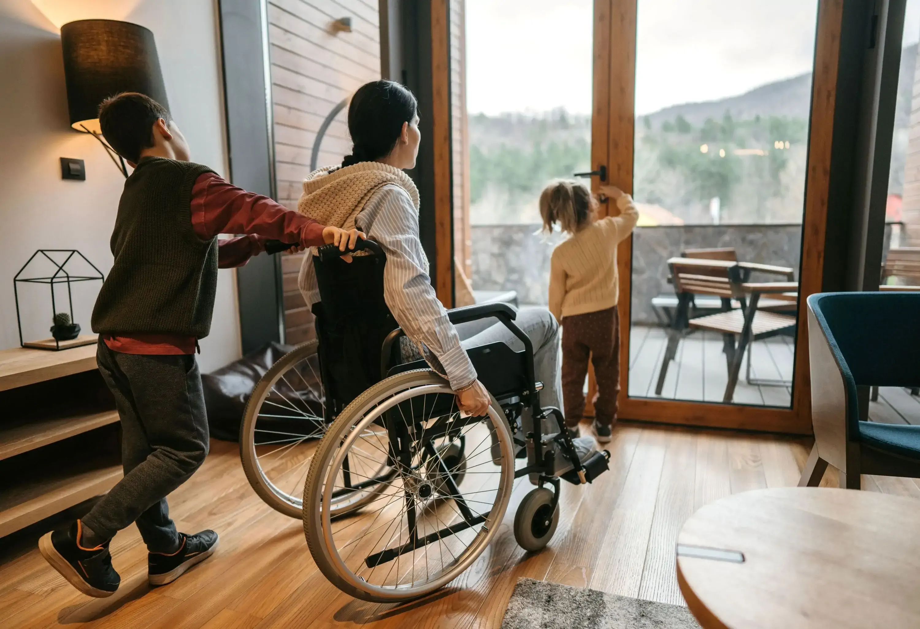Little son and daughter helping their disabled mother in wheelchair to go out on the terrace