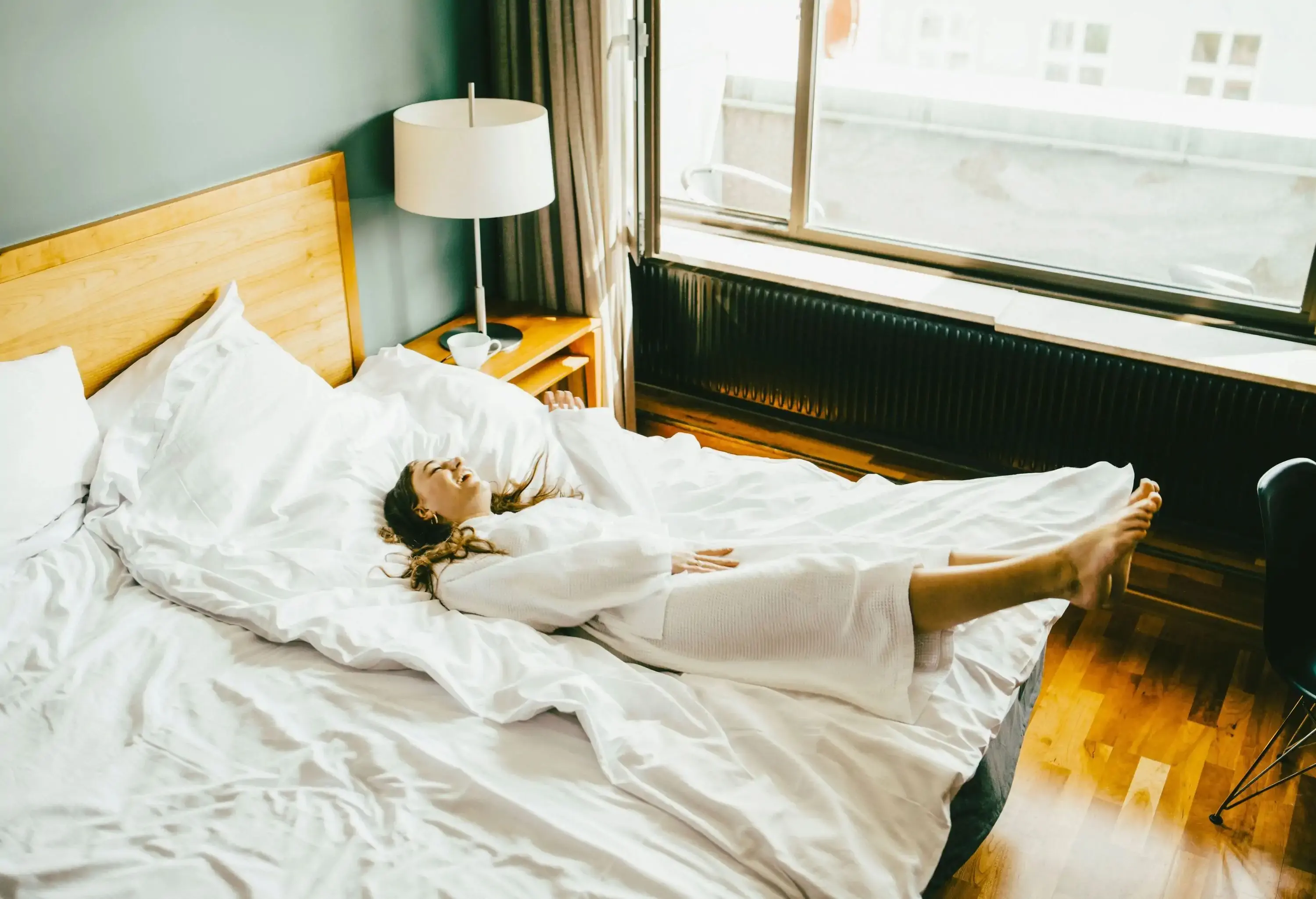 A brunette woman in a bathrobe lies on a bed of a hotel room.