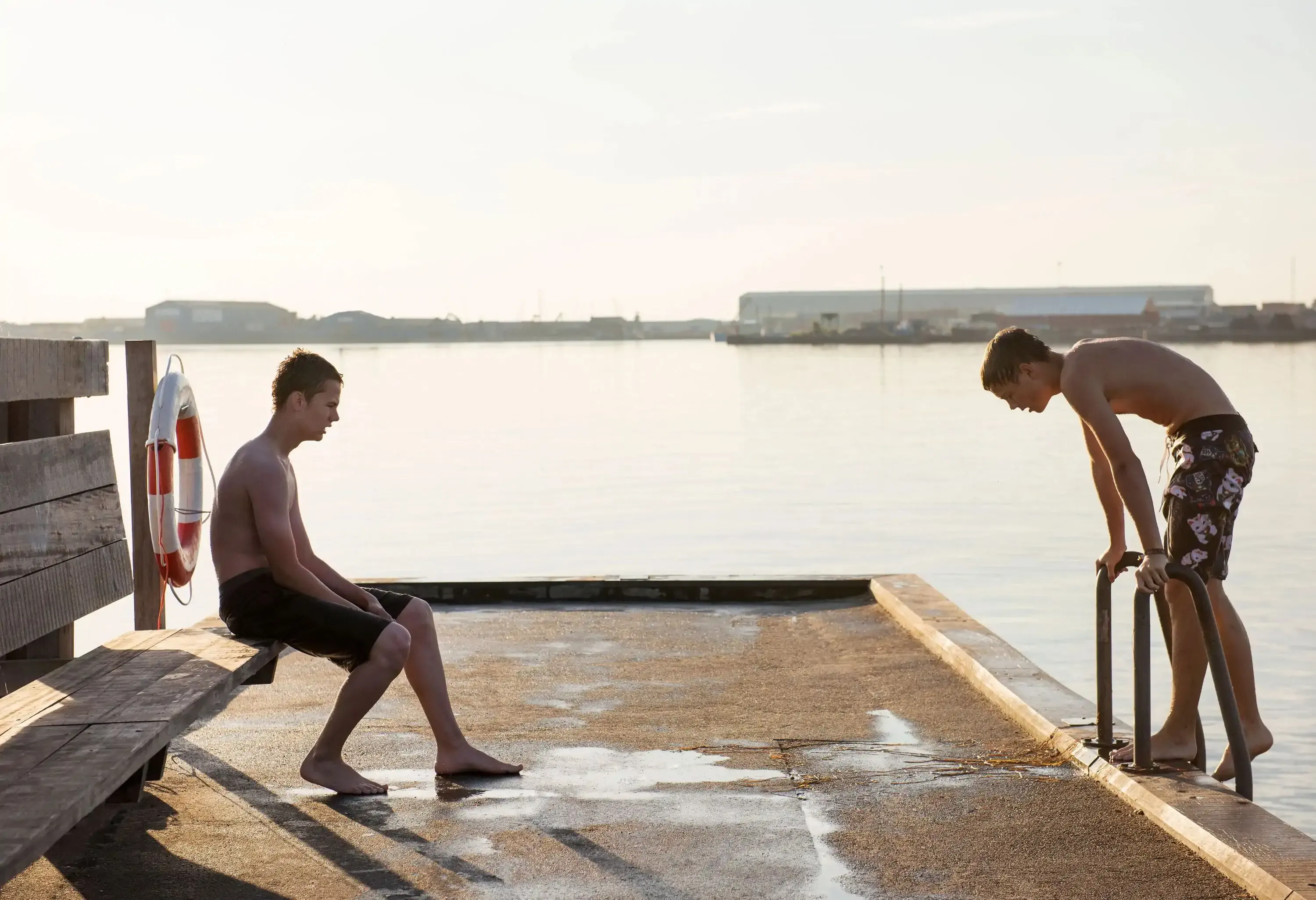 Two half-naked friends take a break from swimming in a harbour.