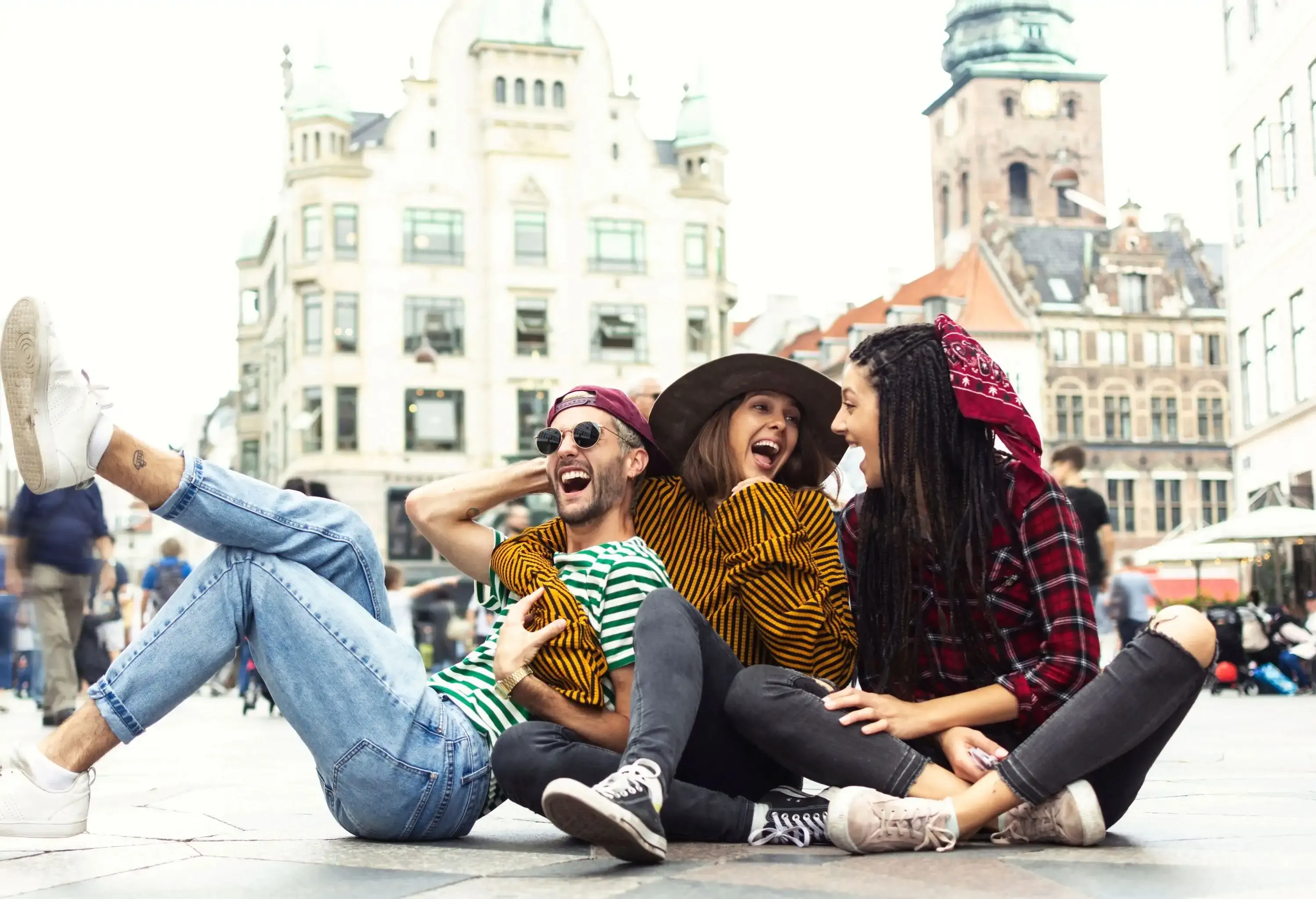 Three friends laughing together as they sit on the floor of a plaza.