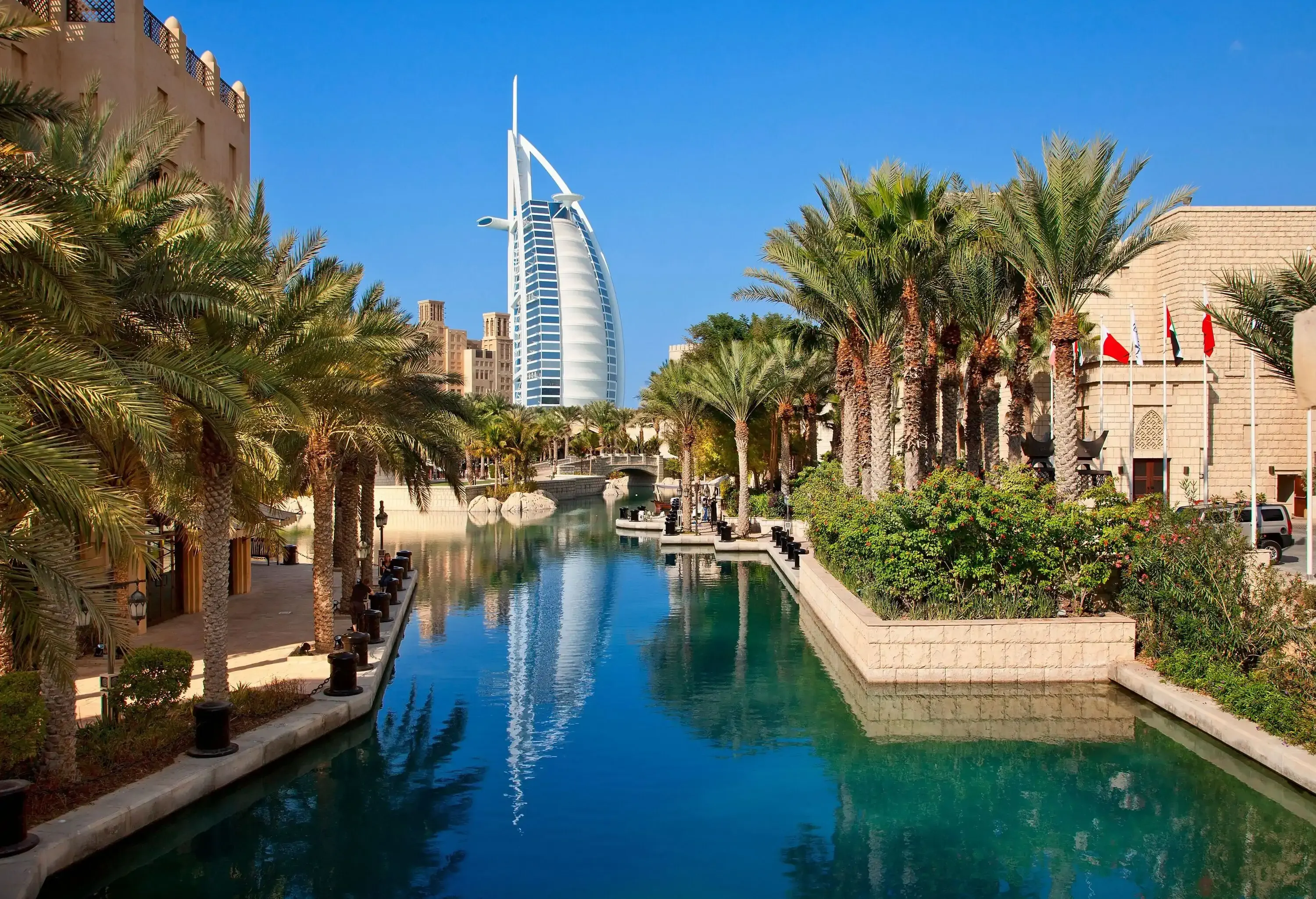 A canal surrounded by concrete banks and palm trees, with a breathtaking view of a contemporary skyscraper in the distance.