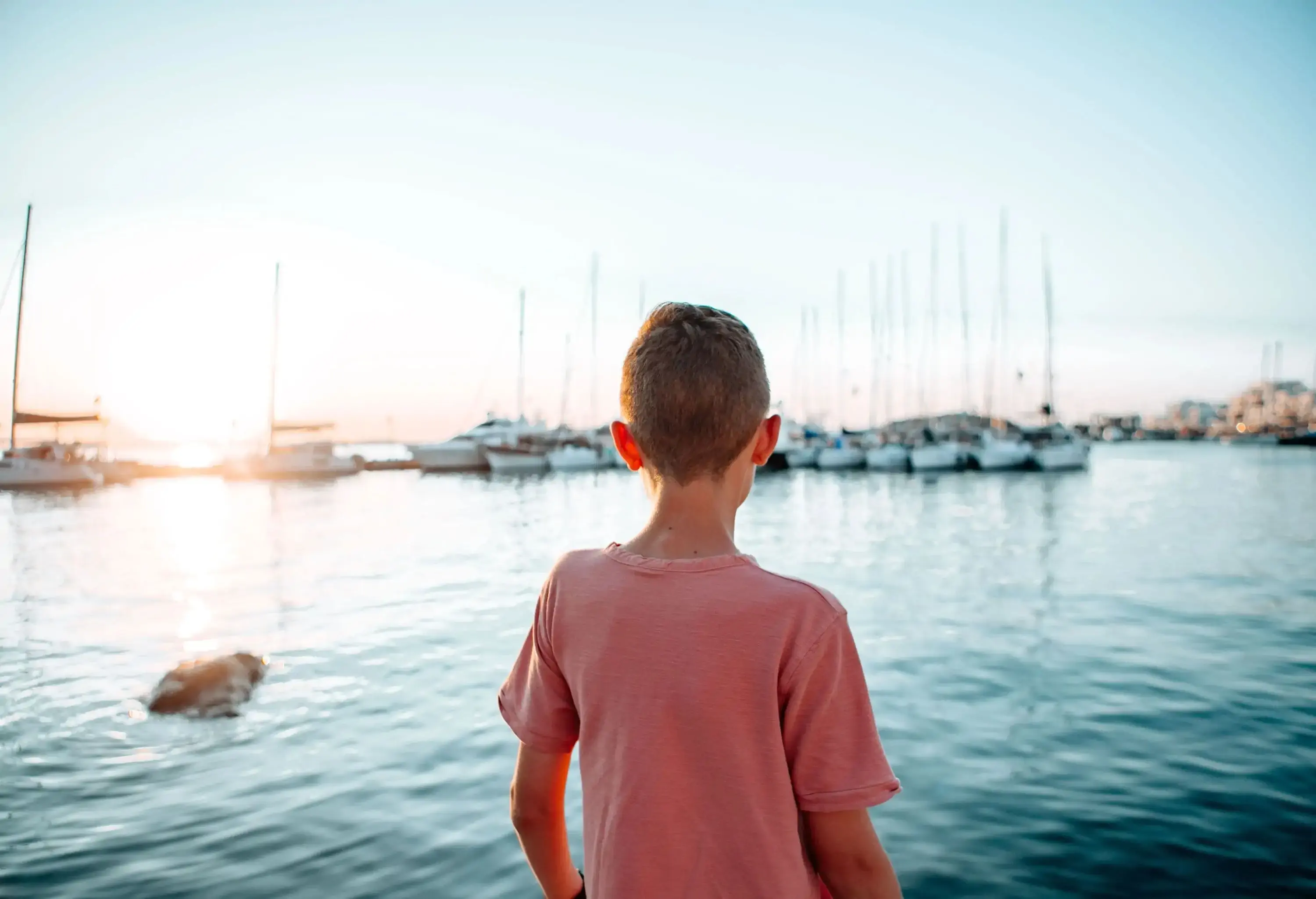 A young boy looking over at the docked boats in a marina.