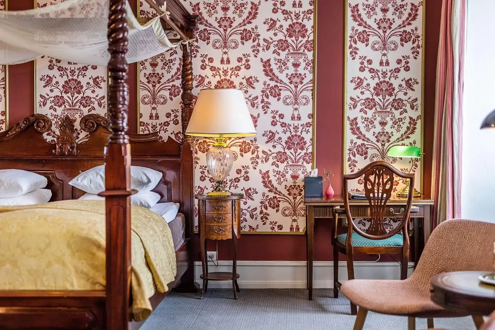 Interior of a traditional castle hotel room with red wallpaper and opulet wooden furniture