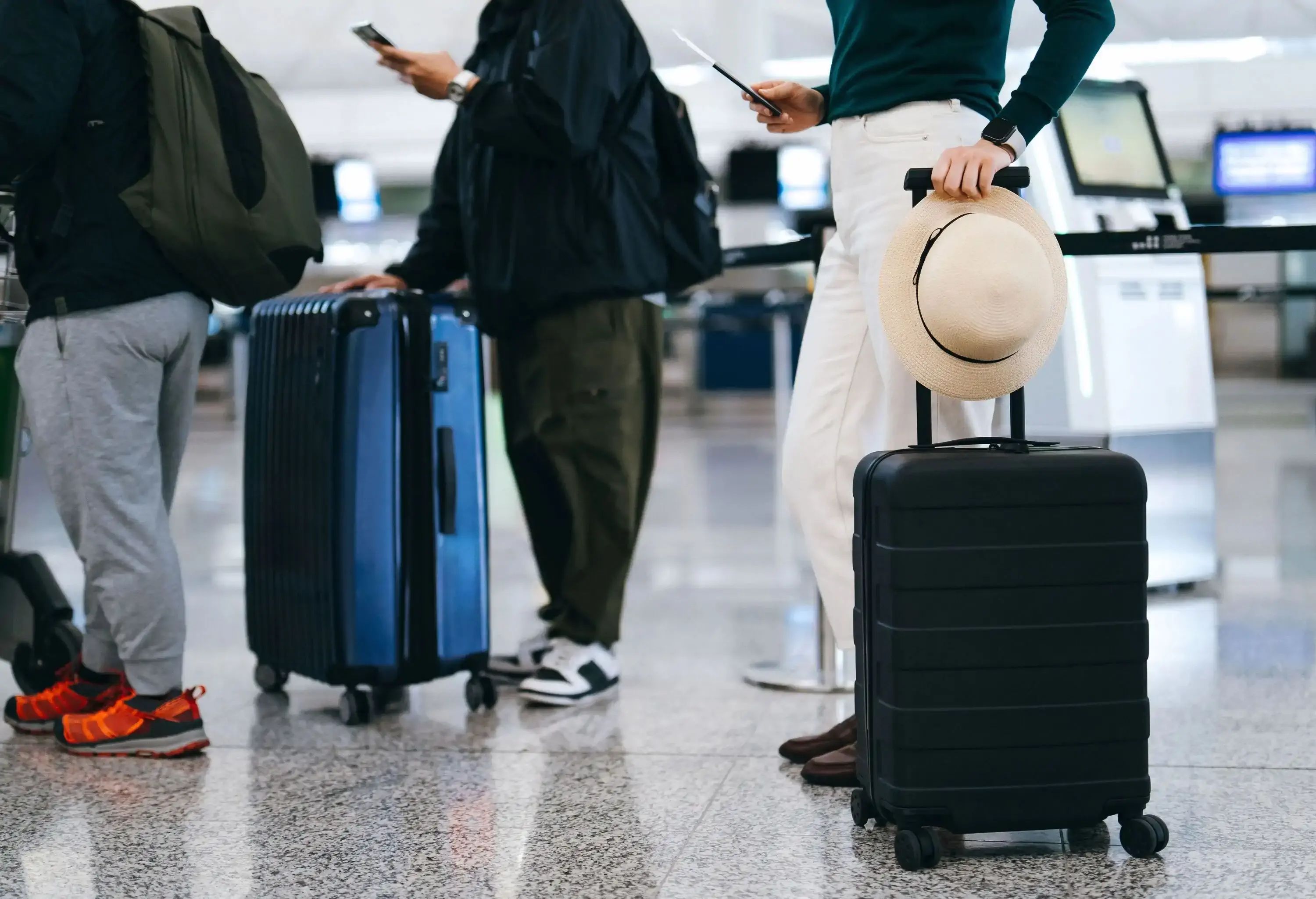 A line of travelers with suitcases and backpacks waiting at an airport terminal.