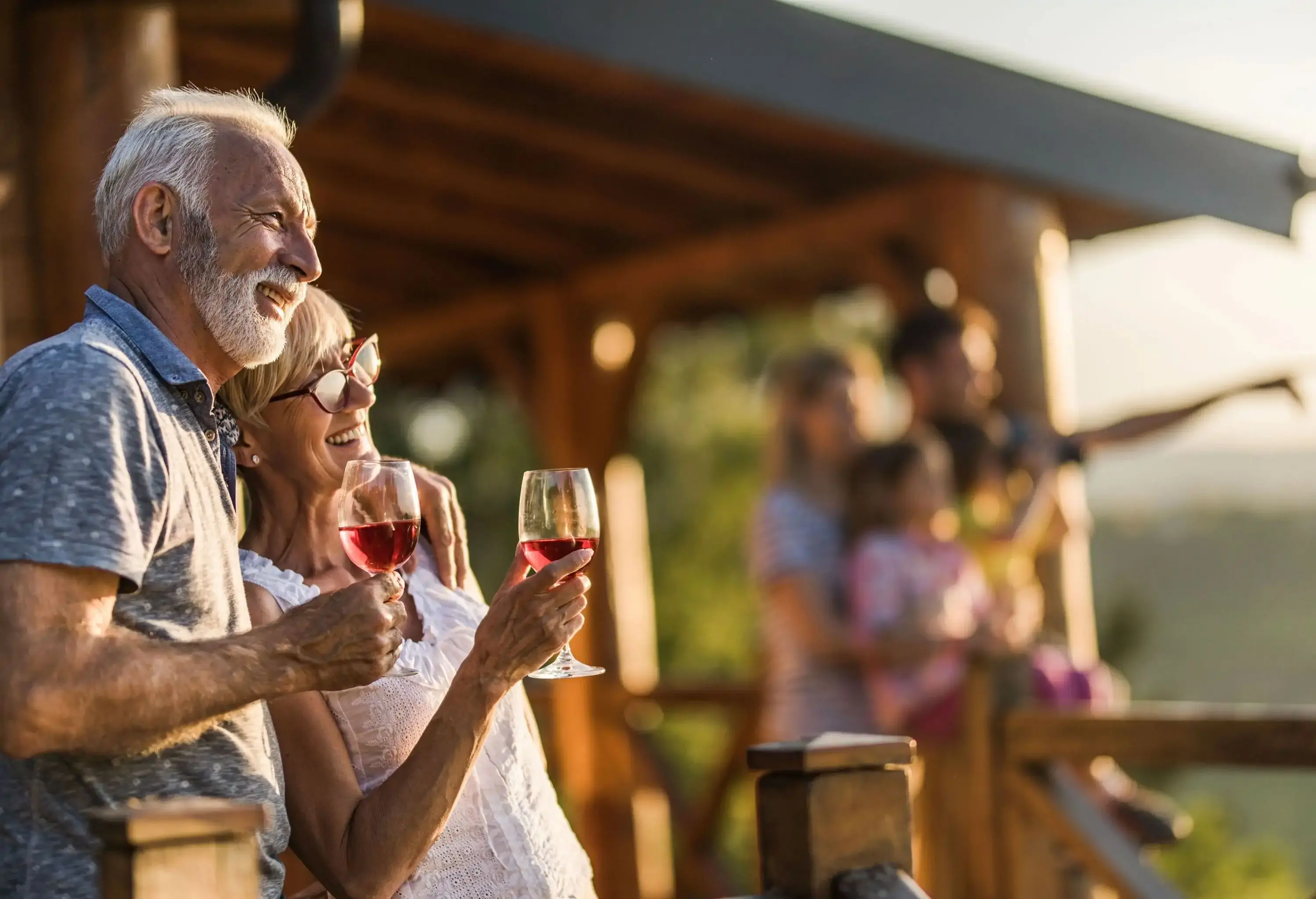 An elderly couple enjoying a glass of wine on their porch with their family.