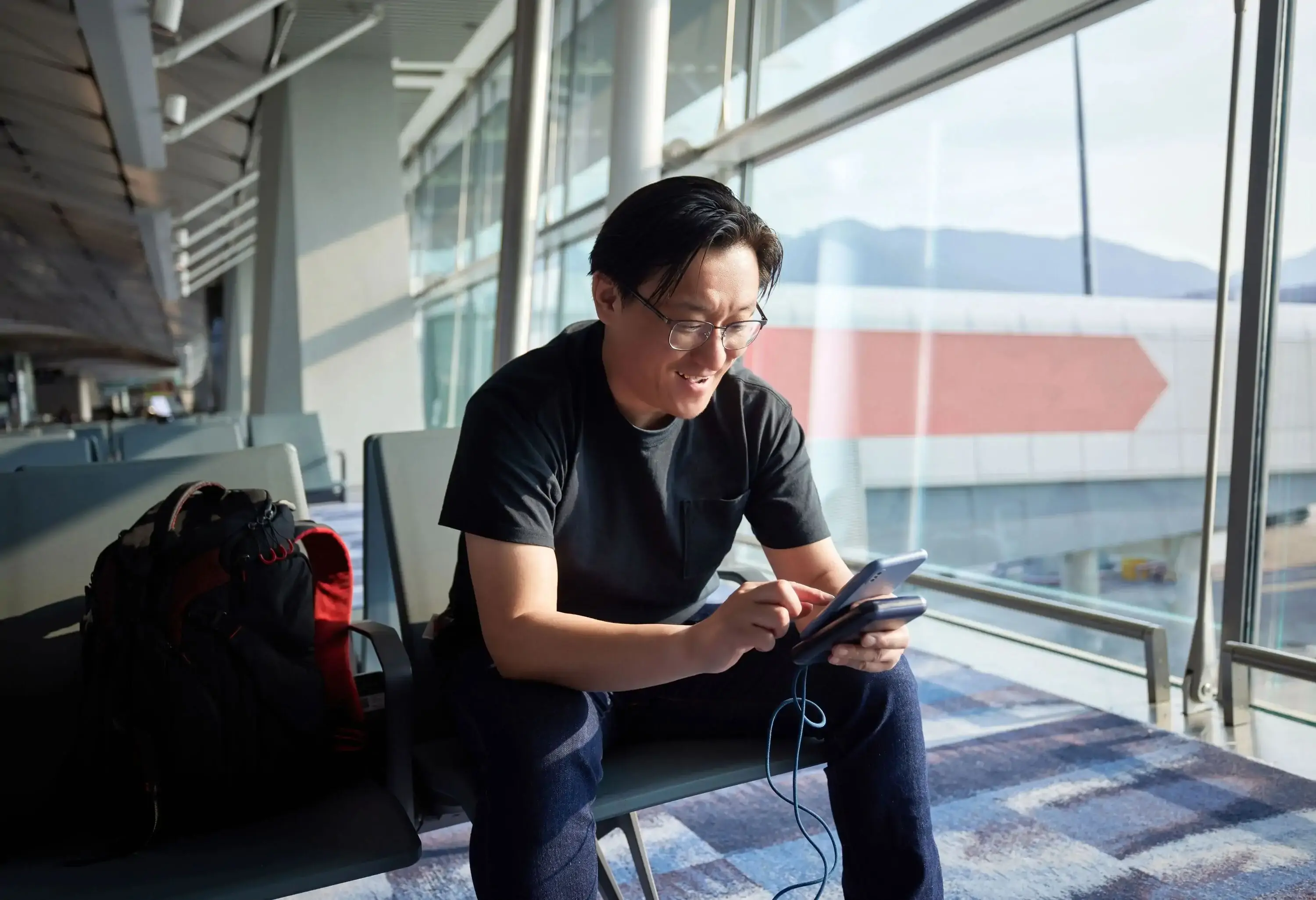 Smiling man holding mobile phone and working in airport.