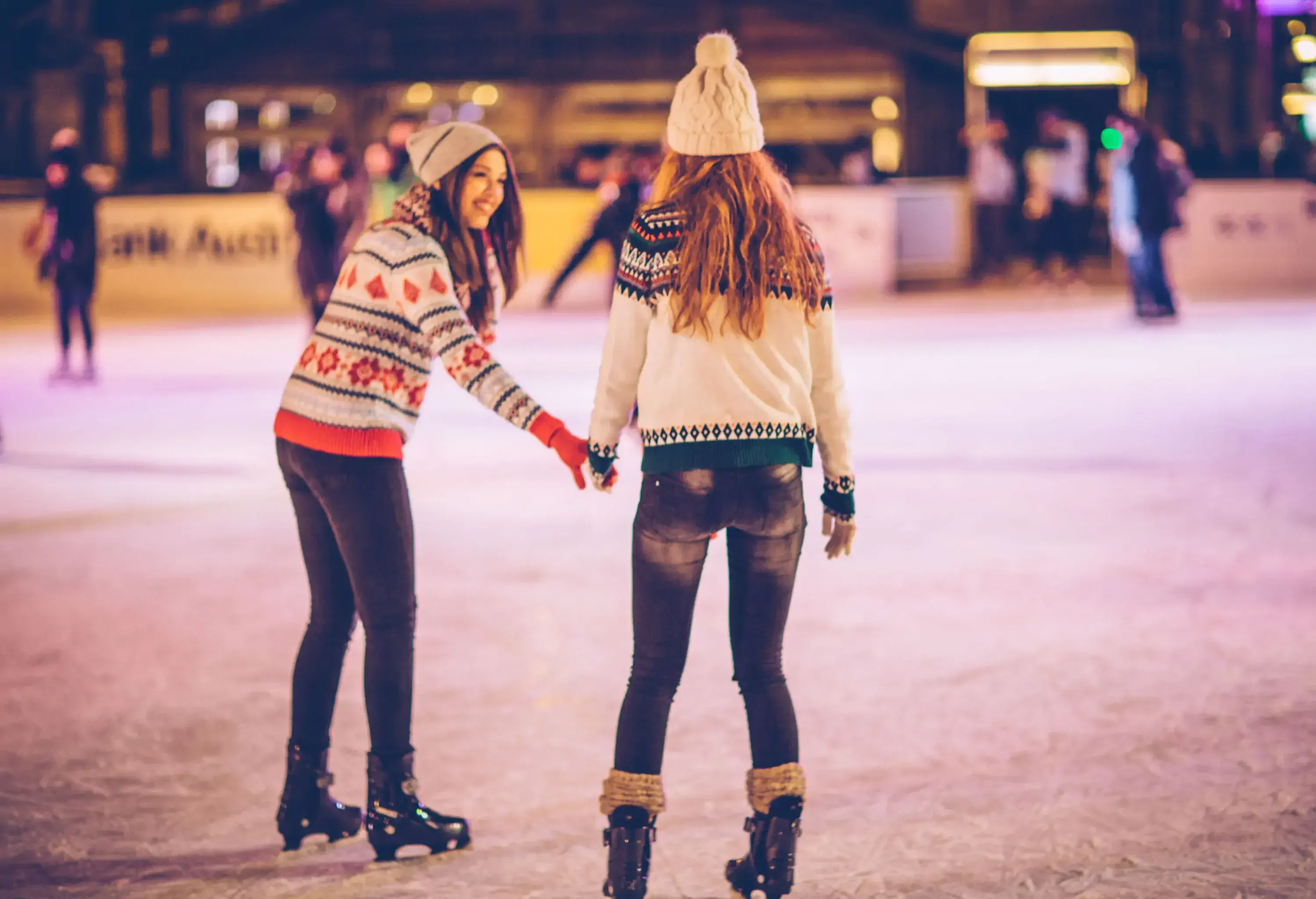 Two female friends enjoying each other's company ice skating in winter.