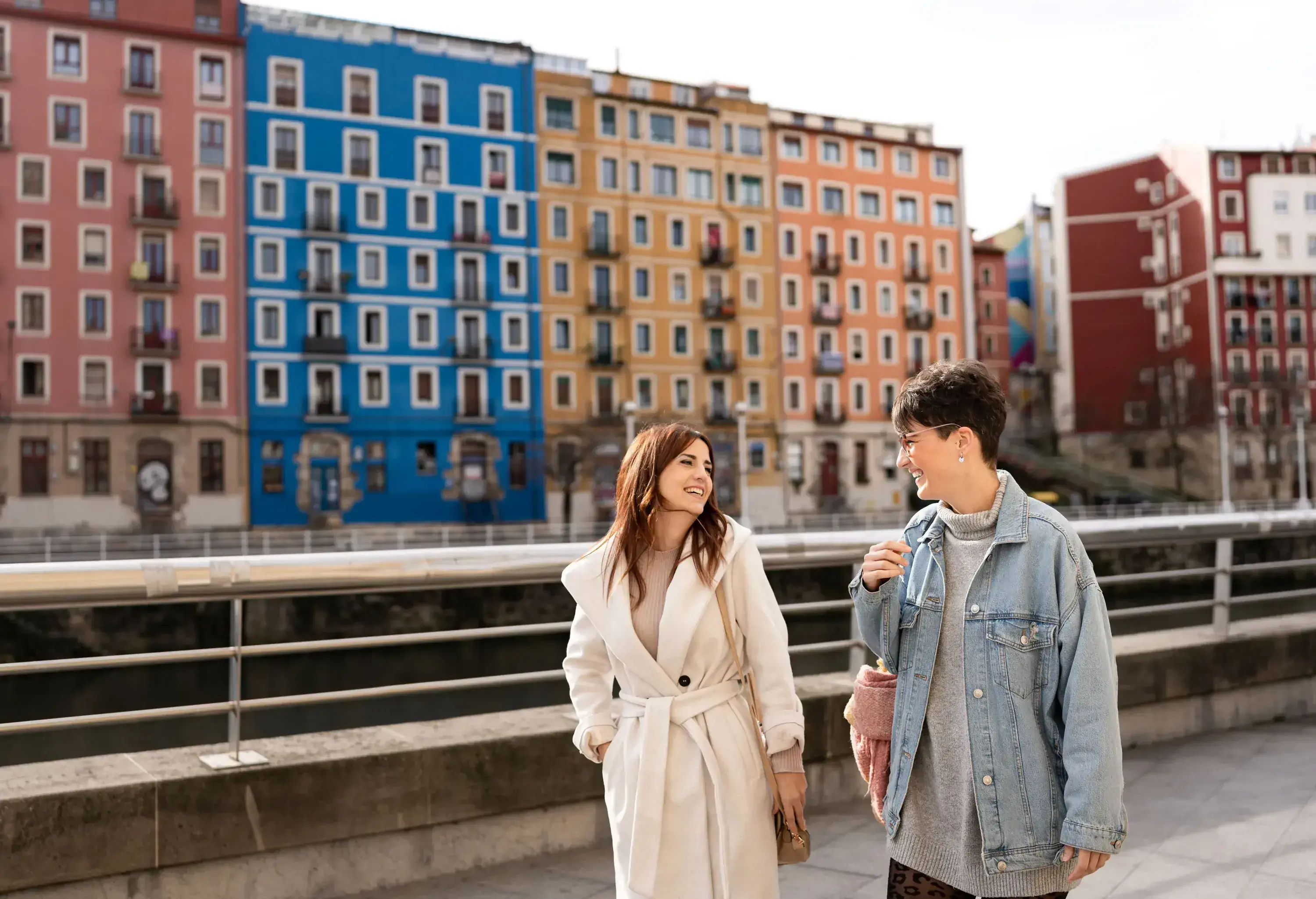 Two woman walking together along a promenade across the colourful buildings.