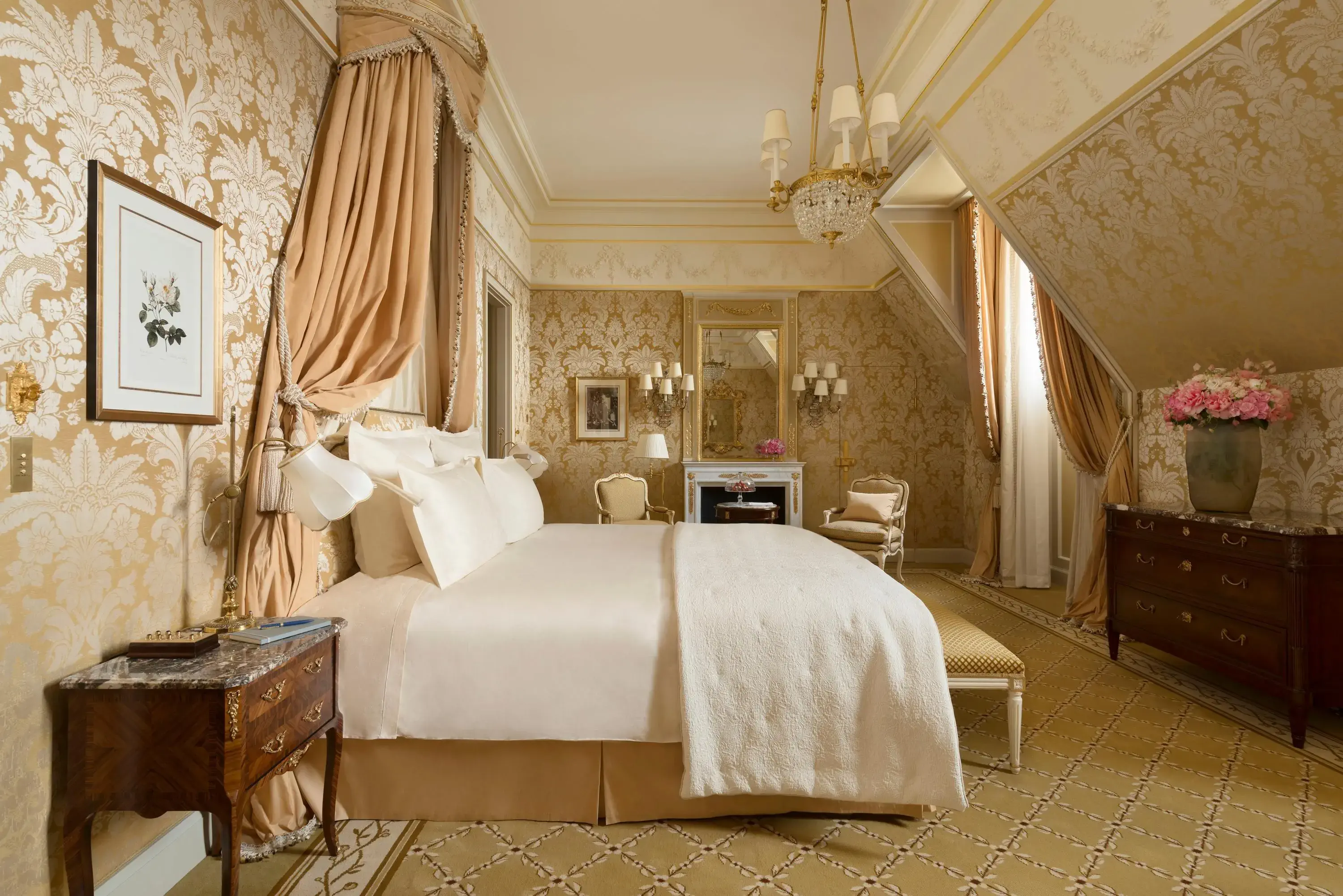 Elegant bedroom with a luxurious canopy bed, ornate beige wallpaper, plush cushions, vintage furniture, and a vase of pink flowers, exuding opulence.