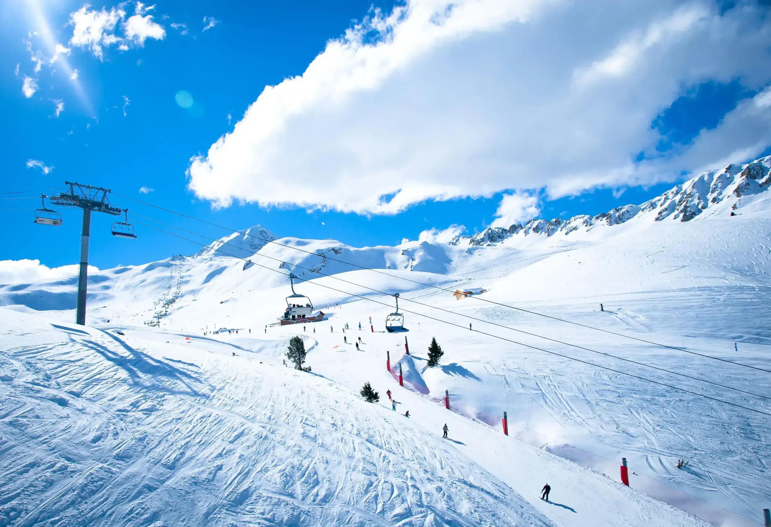 Ski lifts and skiers in sloppy powder snowland with views of mountains covered in deep snow.