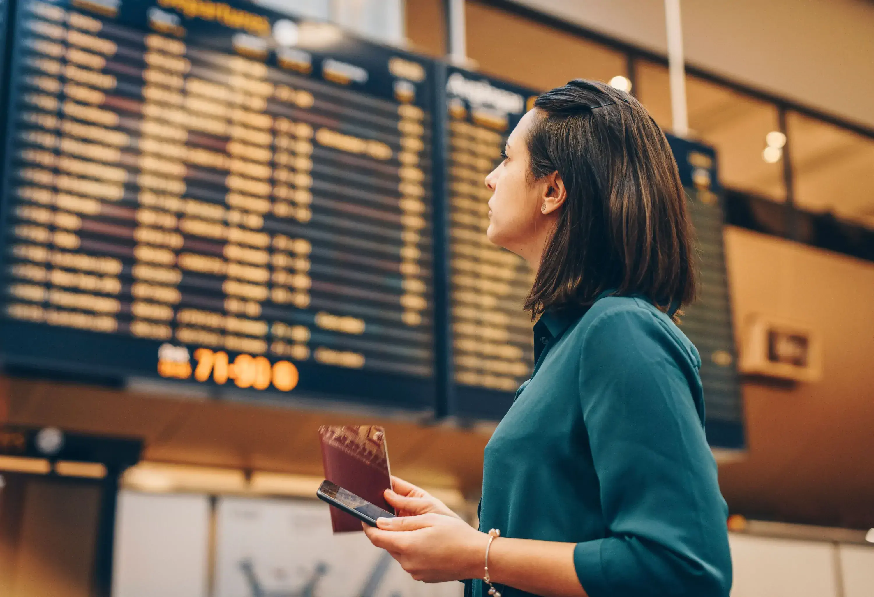 A person looks at a large arrival-departure board while holding a passport and phone.