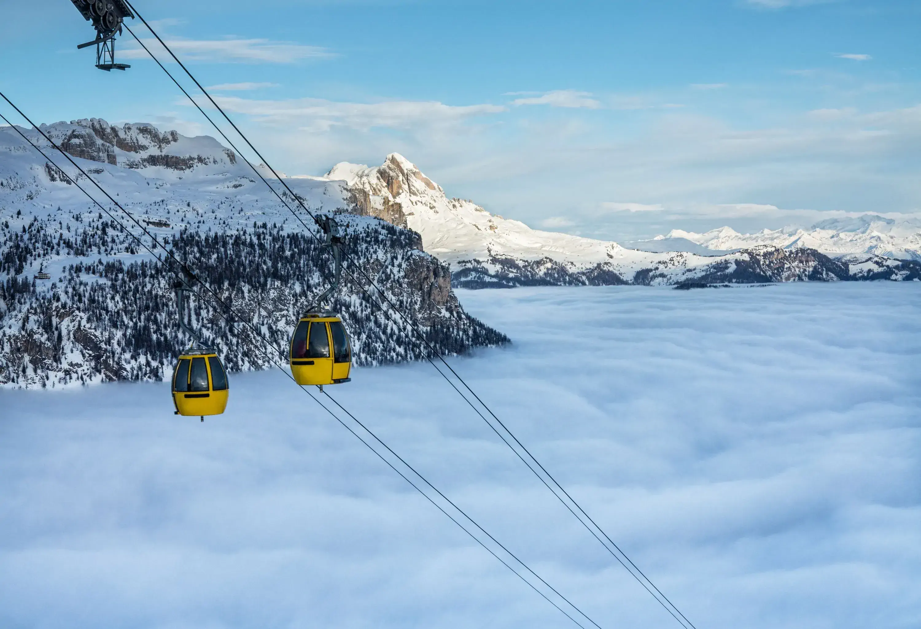 Two yellow cable cars suspended above a blanket of clouds that cover the mountains.