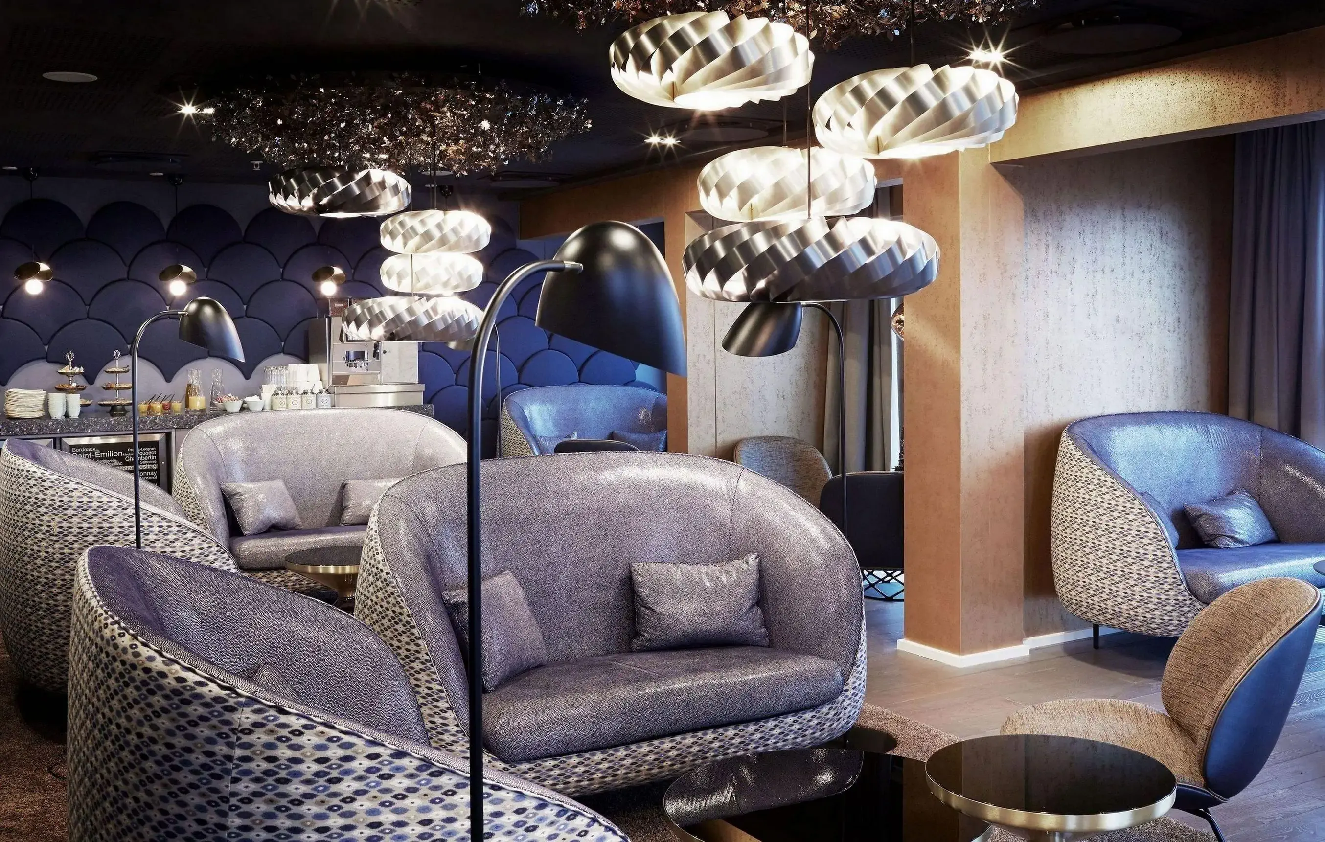 A hotel breakfast room with buffet in the back furnished with futuristic retro sofas and shimmering decorations