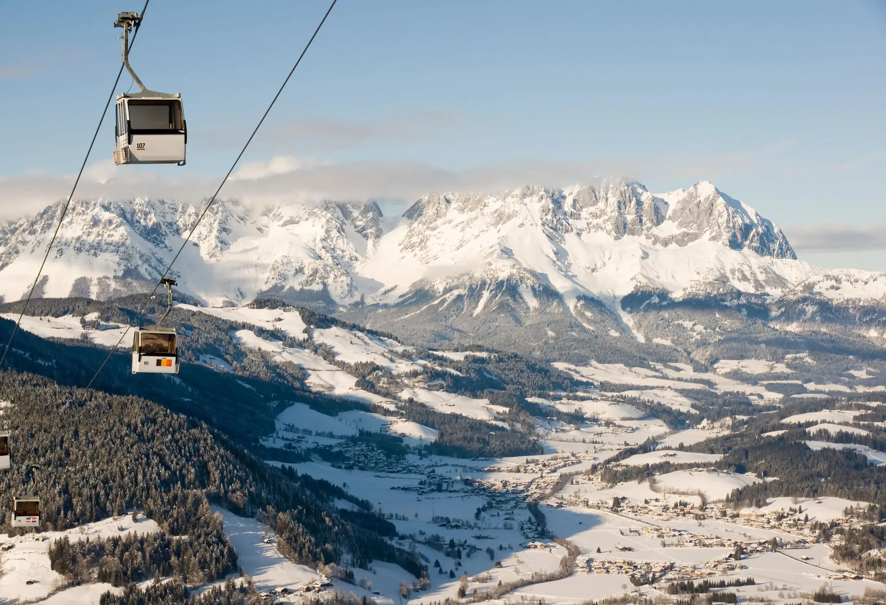 Cable cars over a snowy landscape with trees and a jagged mountain range in the distance.