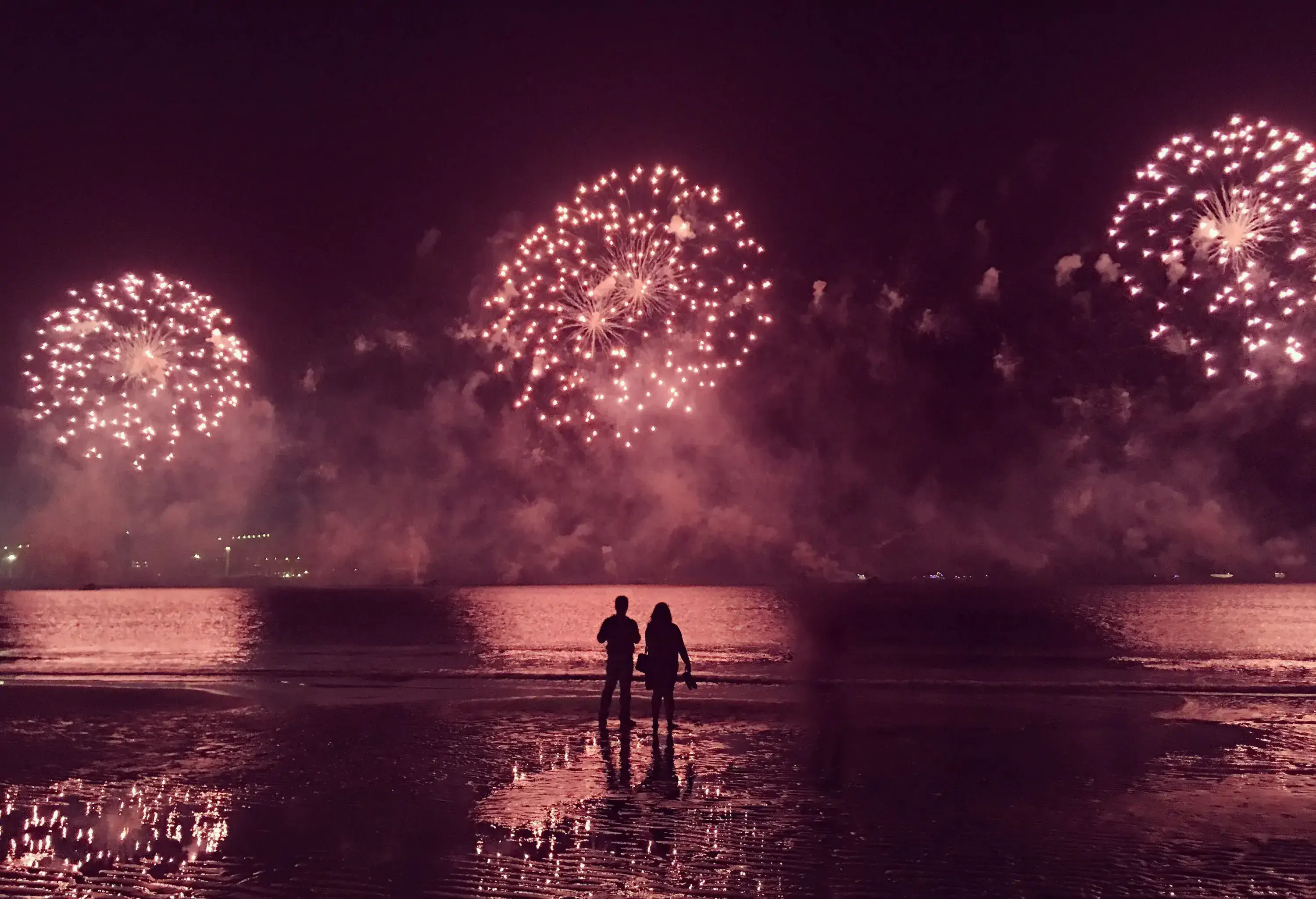 A couple is standing watching the fireworks exploding in the air.