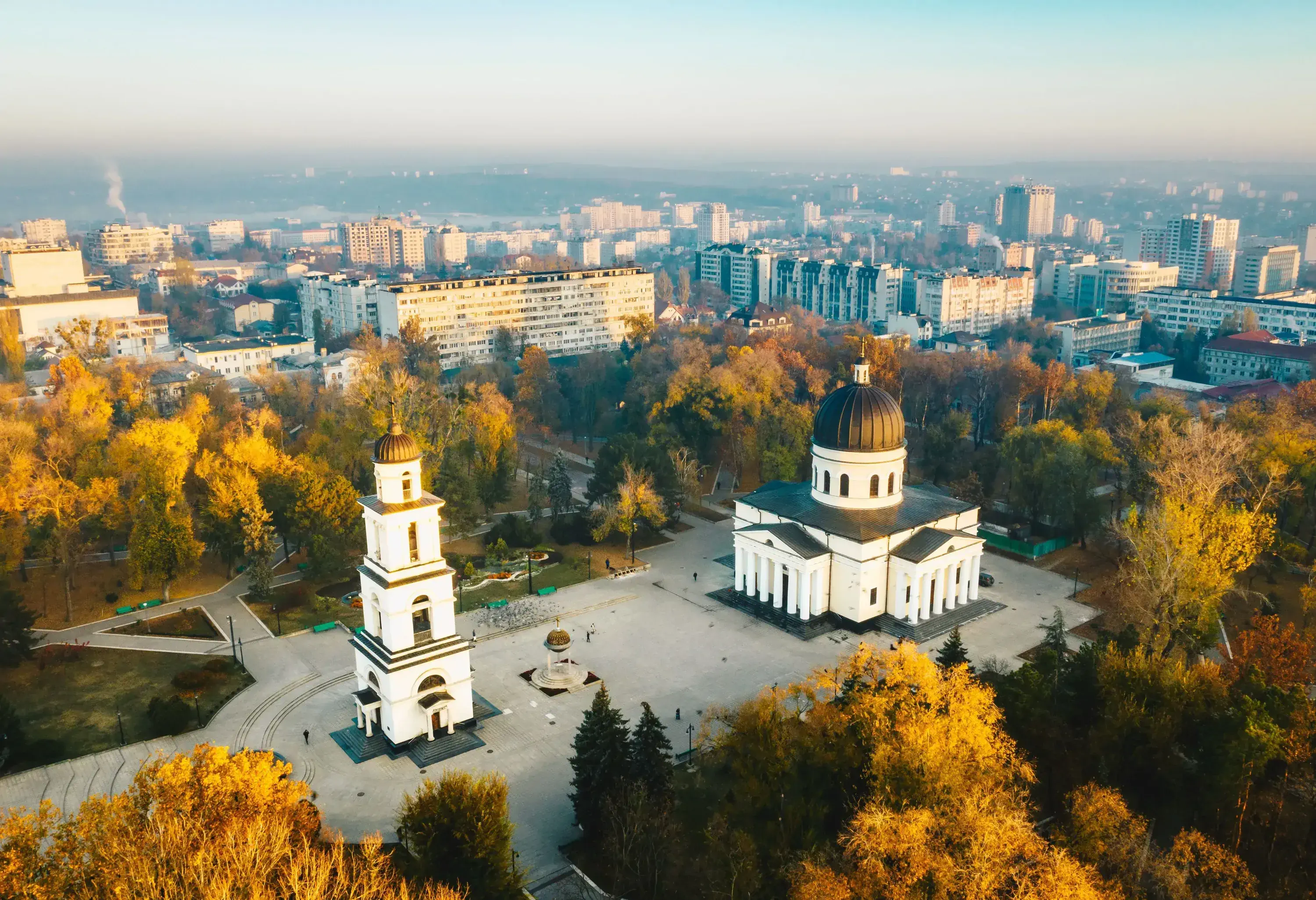 A Neoclassical cathedral facing its bell tower surrounded by lush trees in the city's centre.