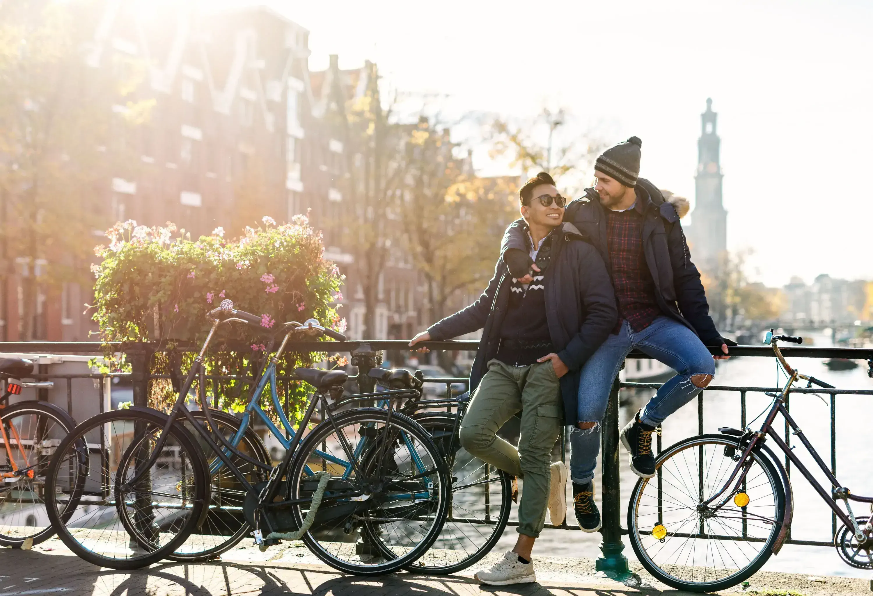 Happy couple on a bridge, one leaning and the other sitting on the railings next to the bicycles.