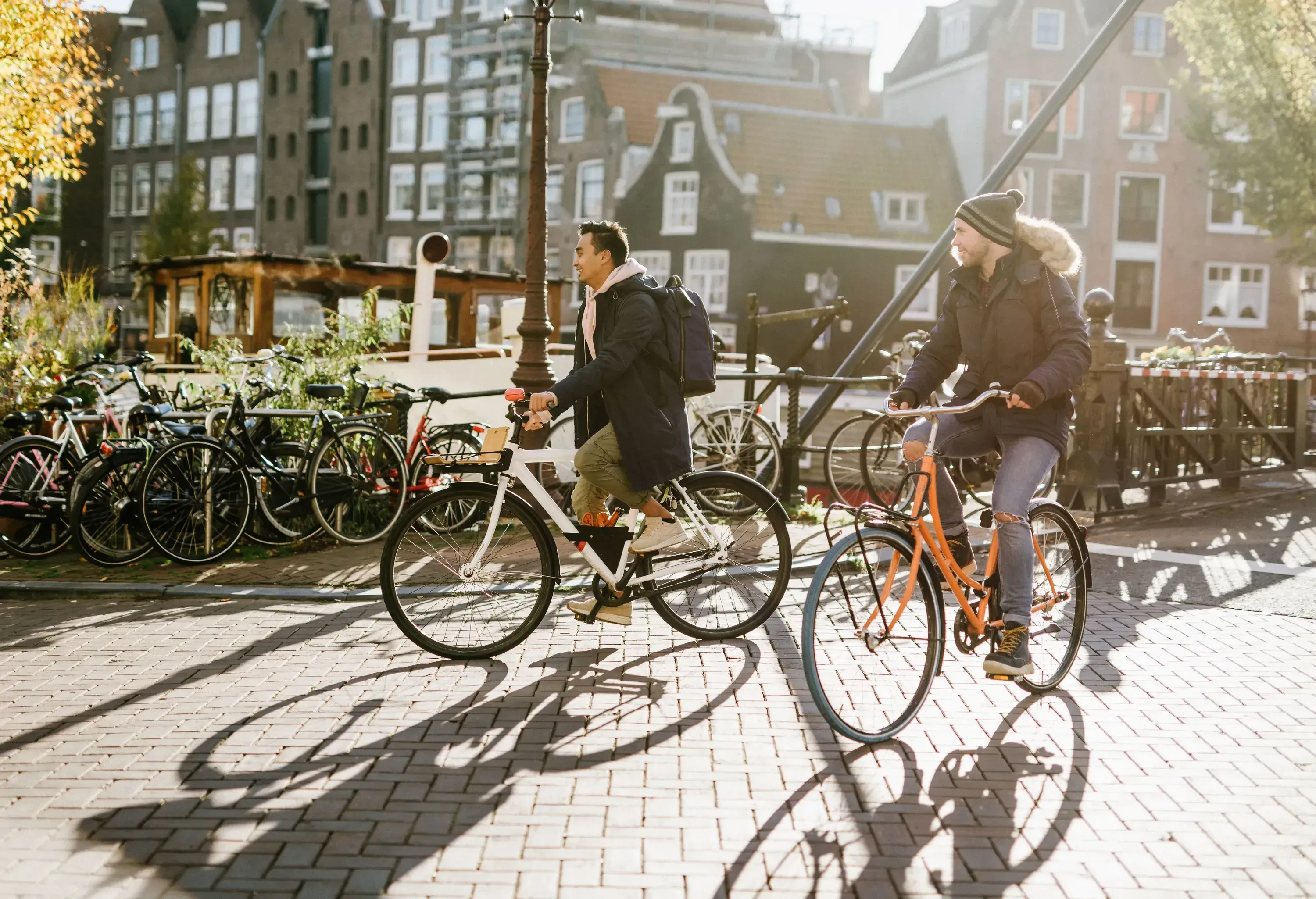 Two people on bicycles, cycling in paved pedestrian and traditional dutch buildings in the background.