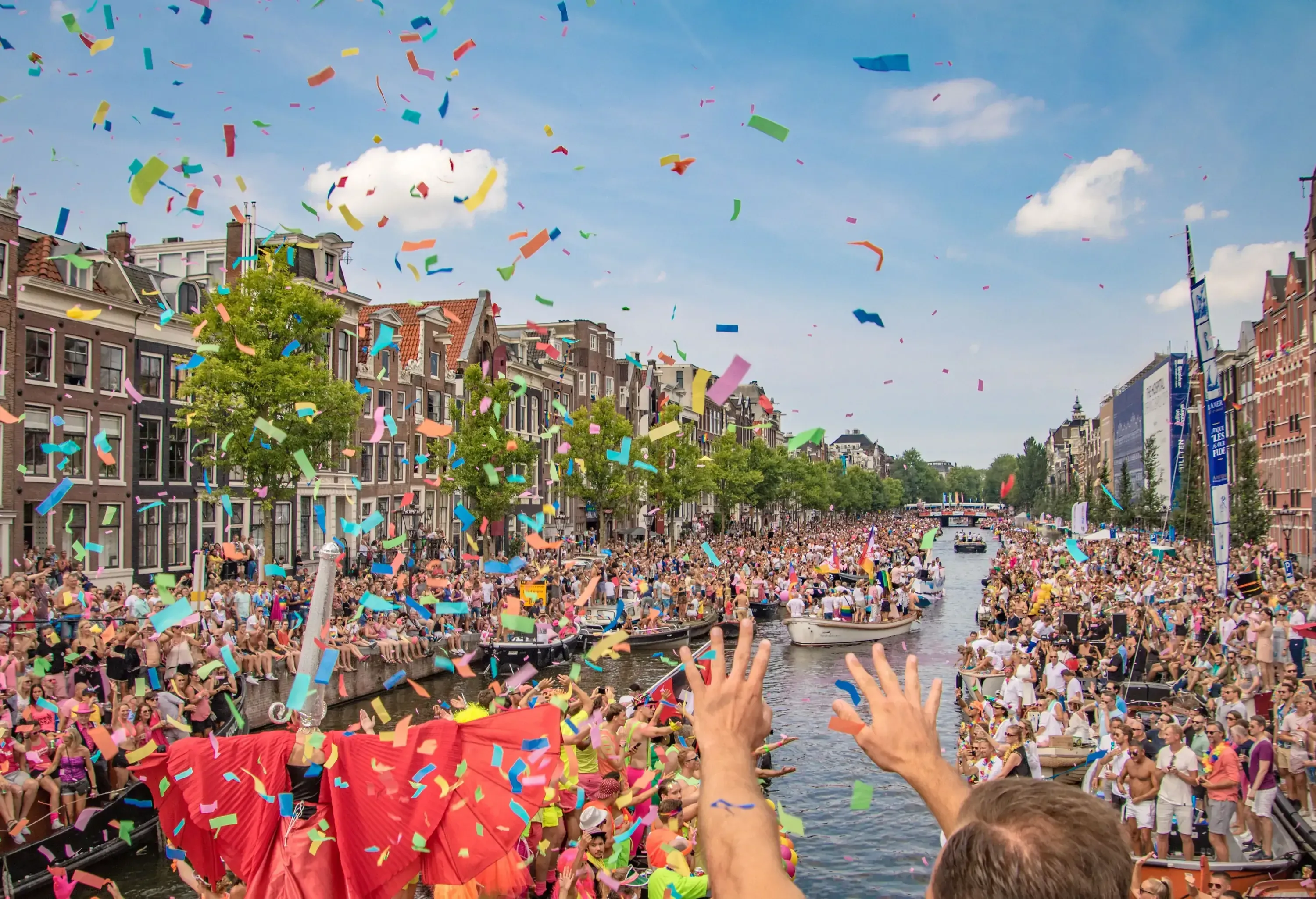 Crowds throw colourful confetti into the canals along Amsterdam's traditional narrow canal houses during the celebration of a festival.