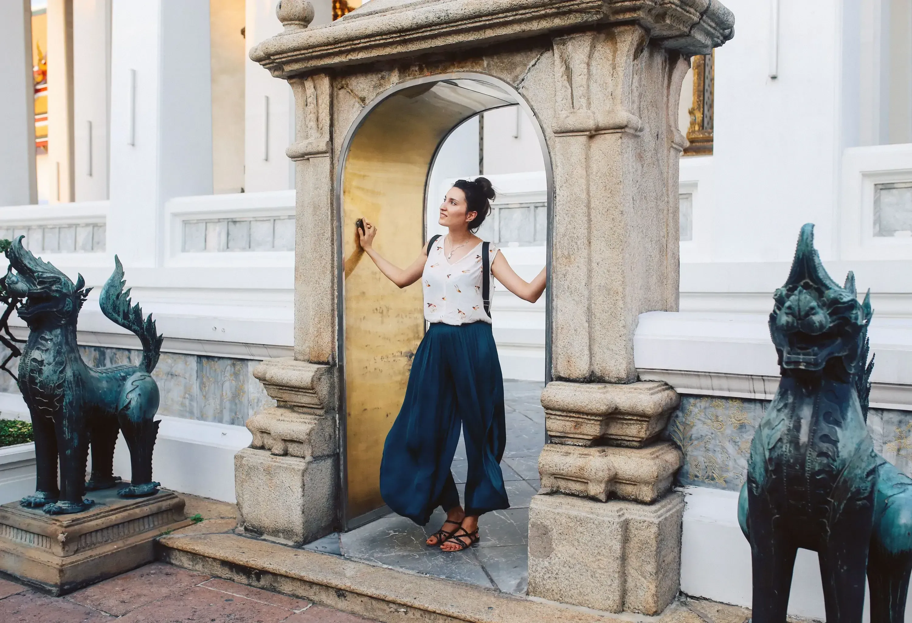 A woman stands under an arched concrete gate between two mythical statues of lion dragons.