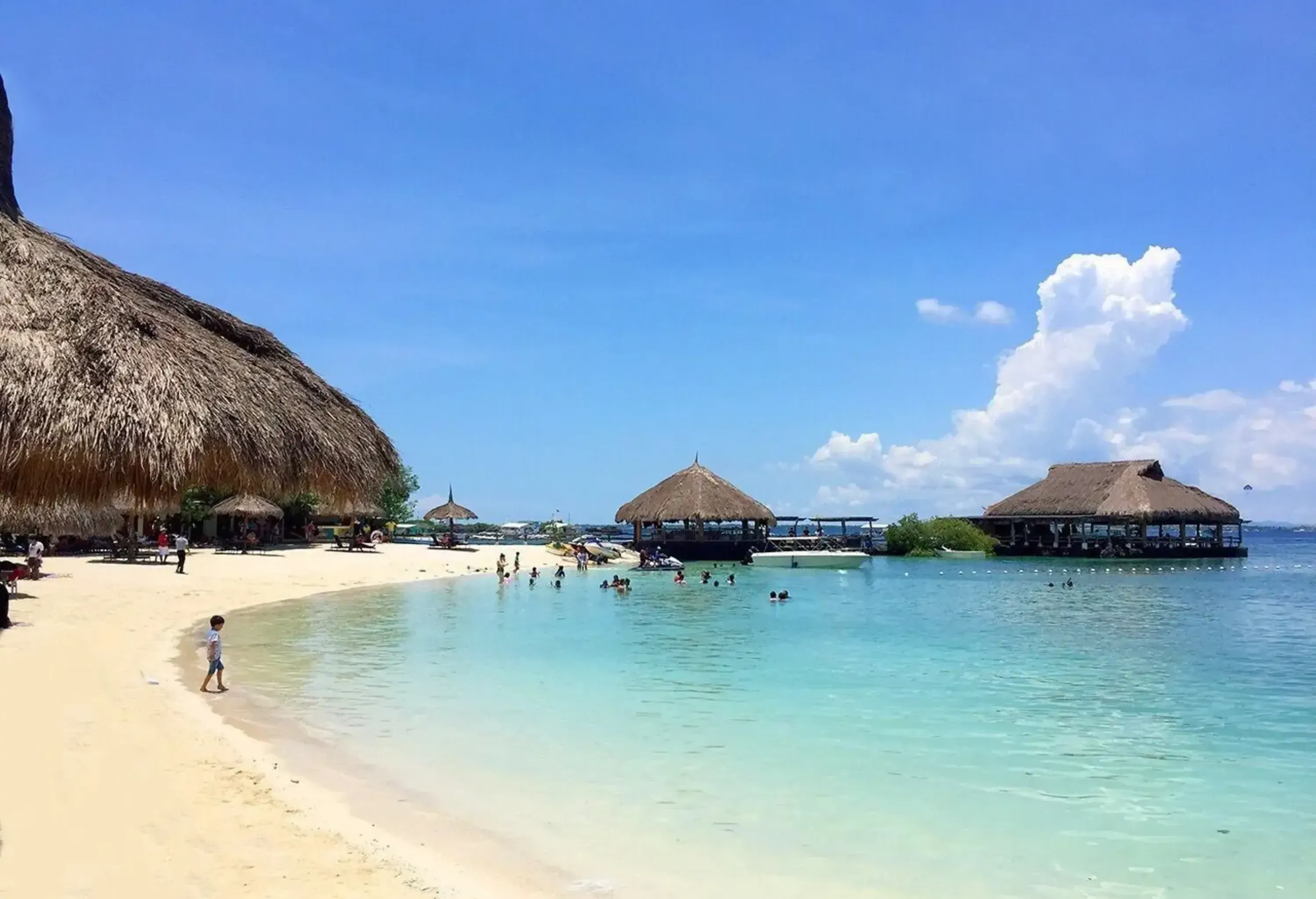A white sand beach resort with cabanas over the beachfront and over the sea.