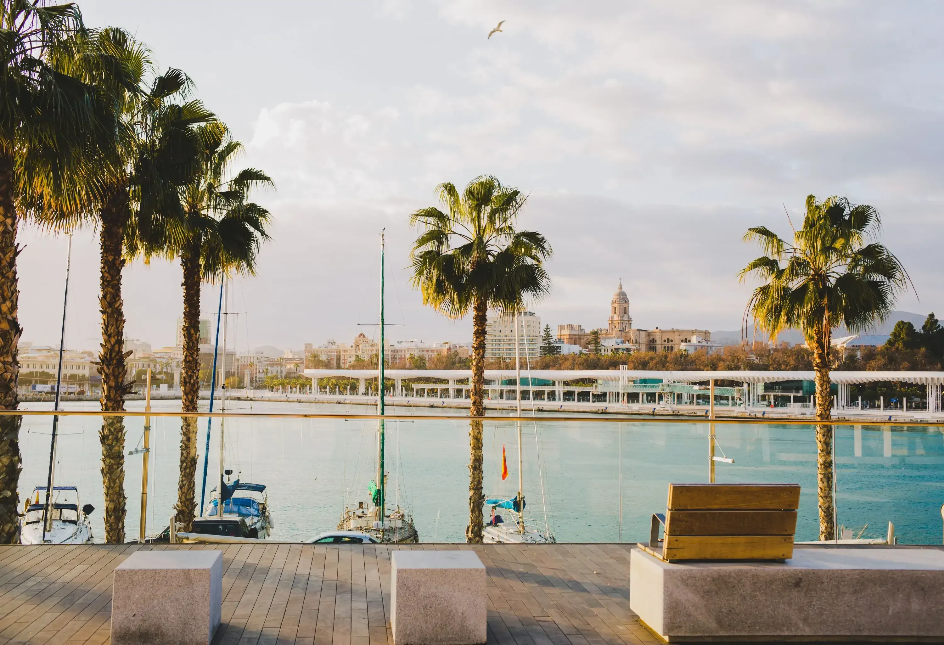 Boats moored in the port with the urban cityscape against the cloudy blue sky seen from the promenade.