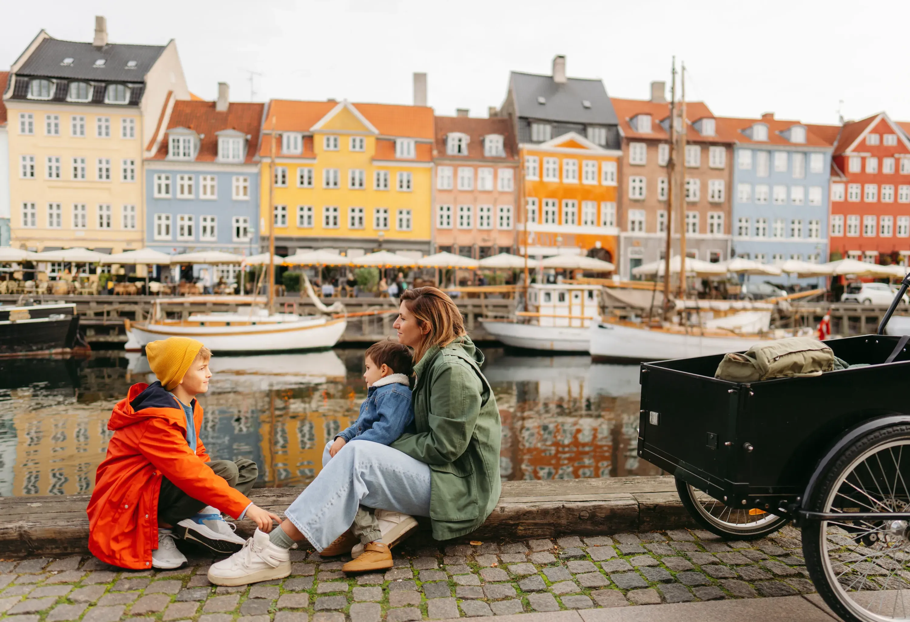 Photo of a young mom with two boys enjoy the view of colourful traditional houses in Nyhavn pier, Copenhagen,  Denmark.
