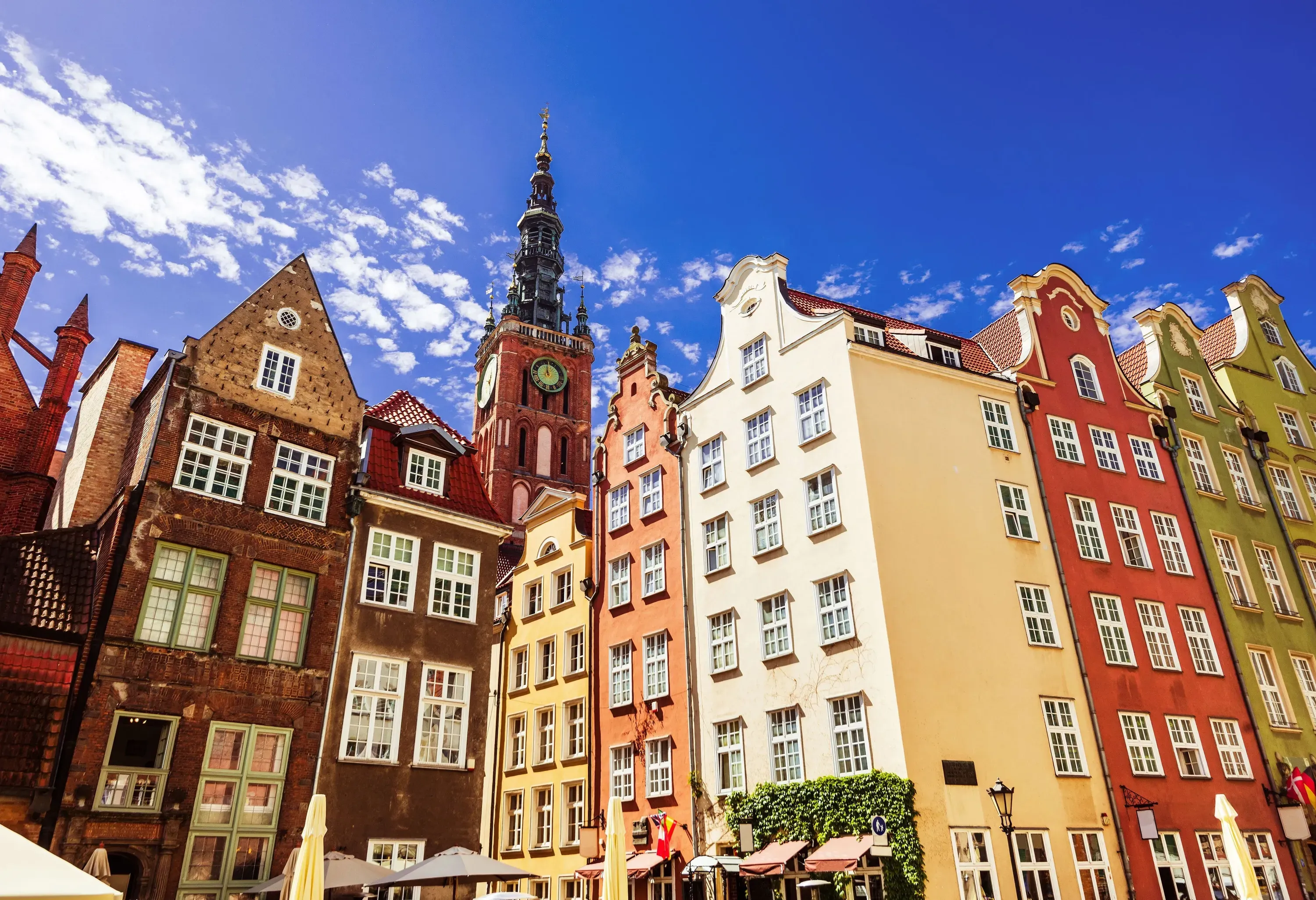 Colourful buildings with Dutch gable roofs and a clock tower rising into the azure sky.