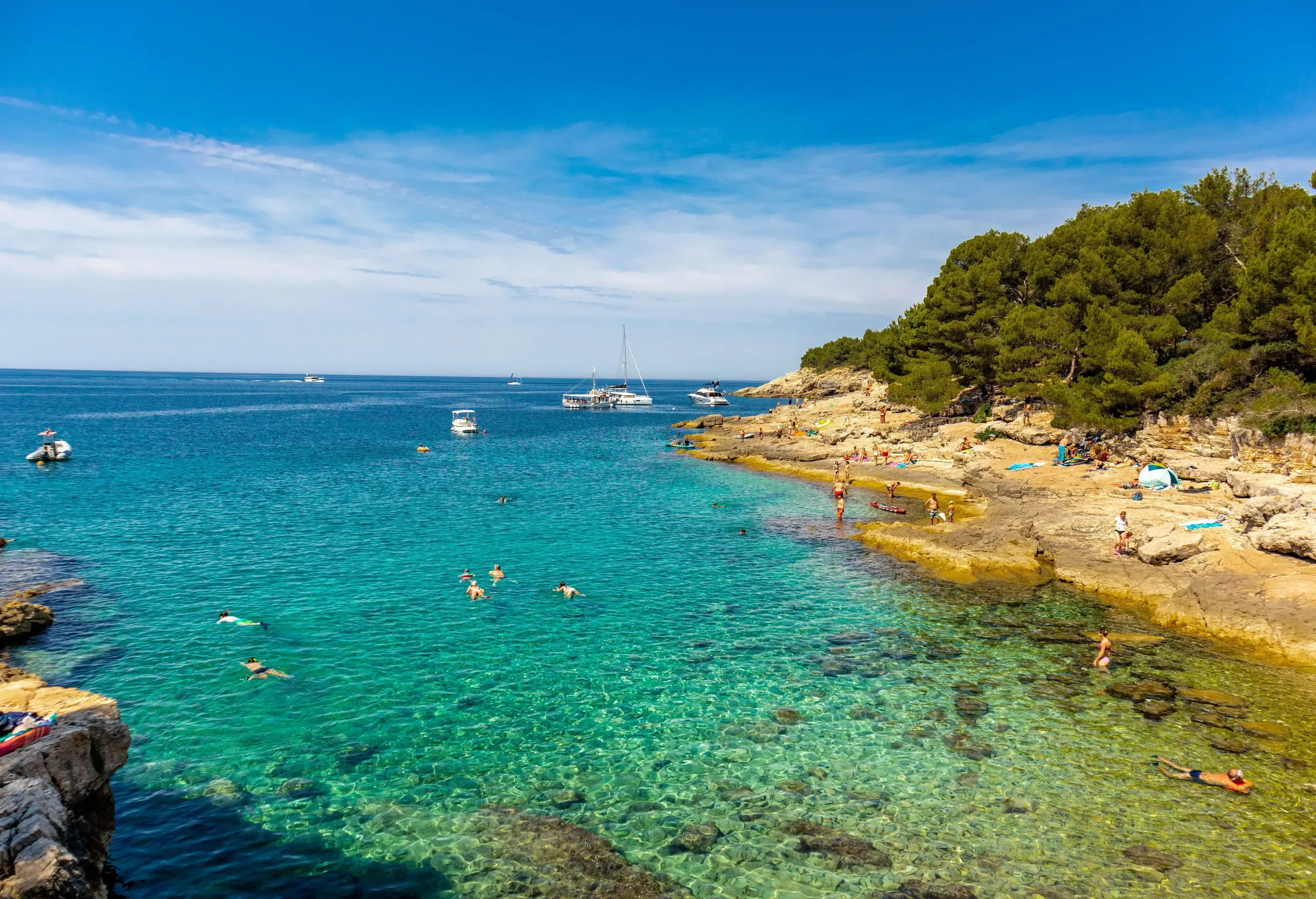 People swimming in the clear waters of a rocky bay.