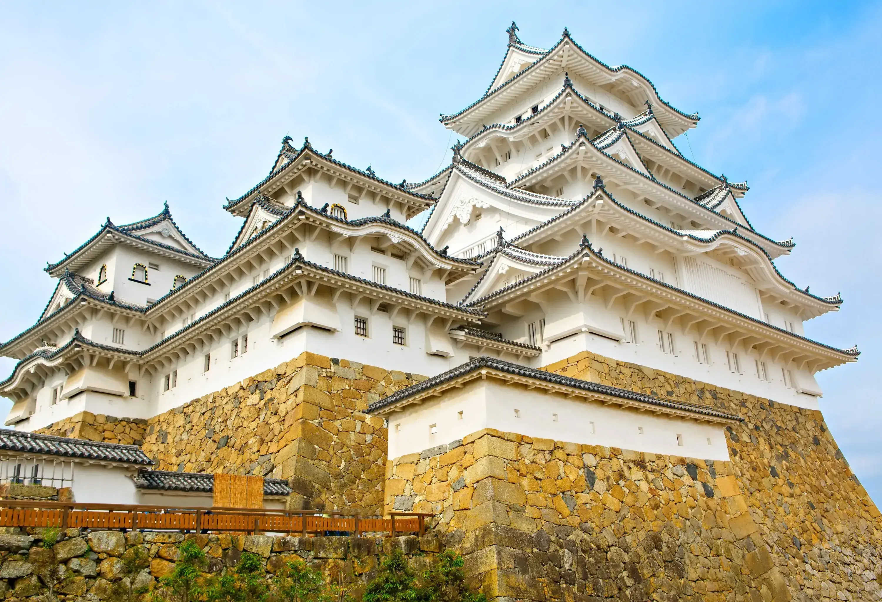 Himeji Castle is a white castle with multiple windows and ceramic tile roofs set on top of piled rocks.