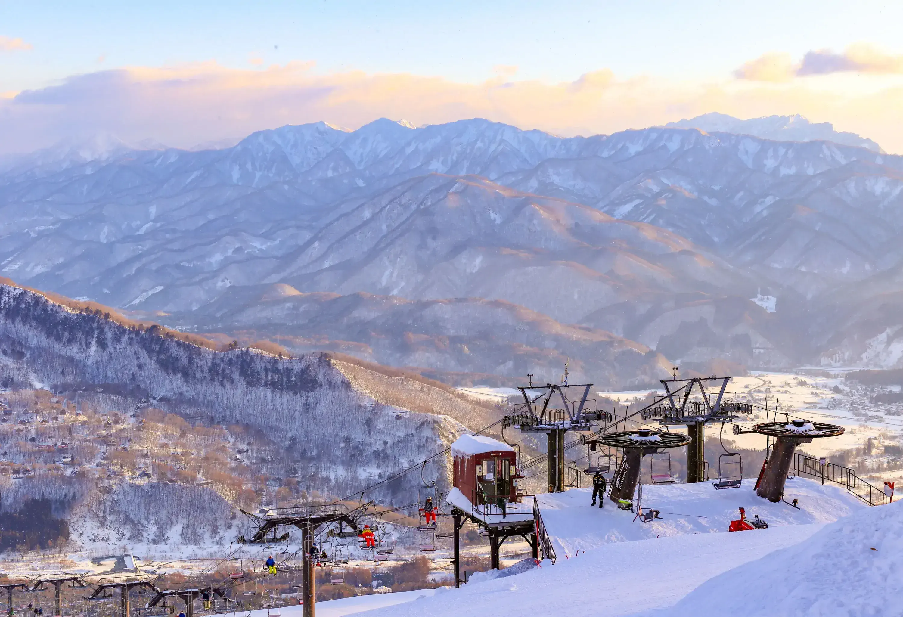 As the chairlift ascends, riders are treated to a stunning view of the snow-covered landscape below, with a majestic mountain range stretching out in the distance.