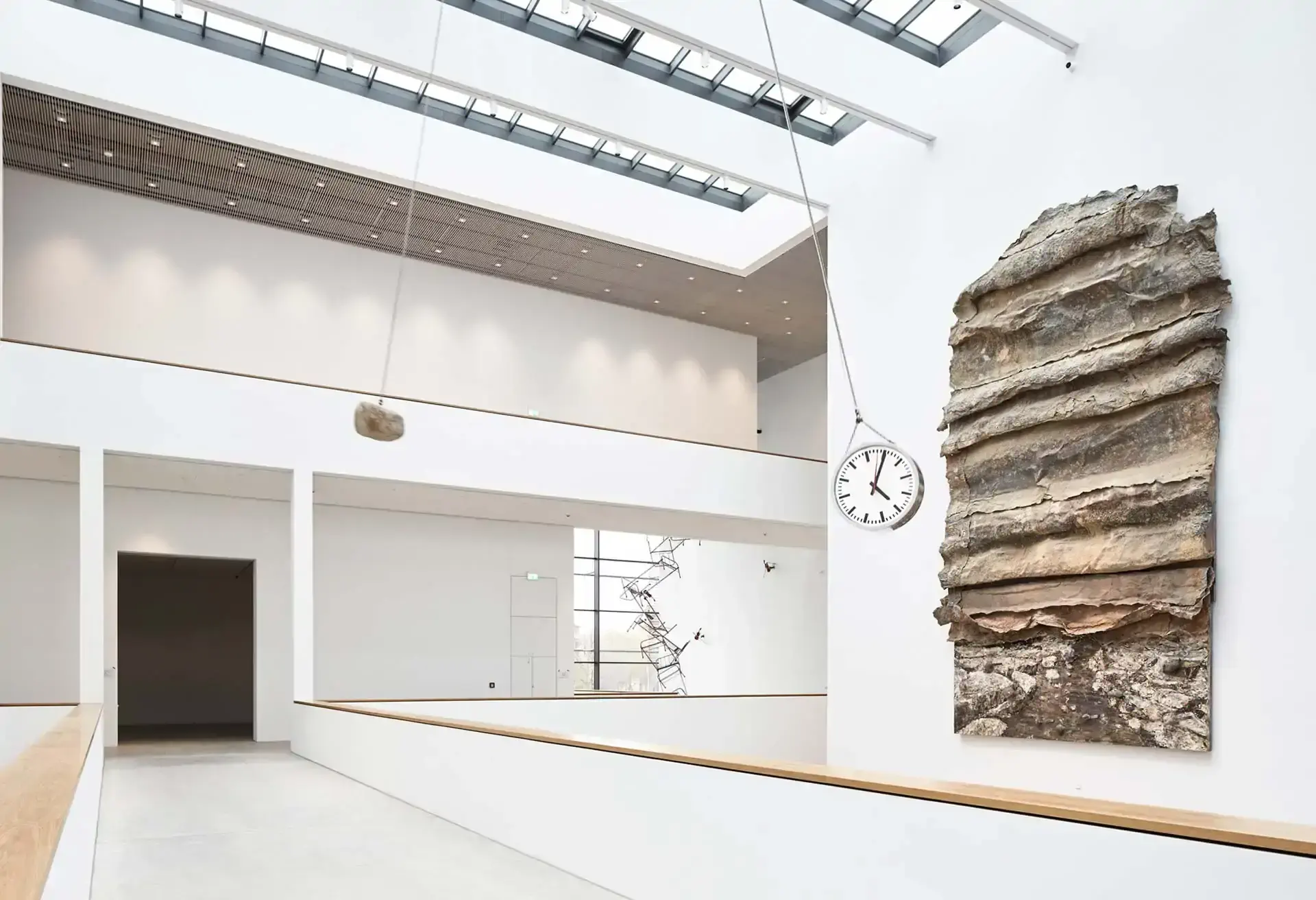 Moderne indendørs udstilling med en stor stenrelief og væguret i et lyst rum.