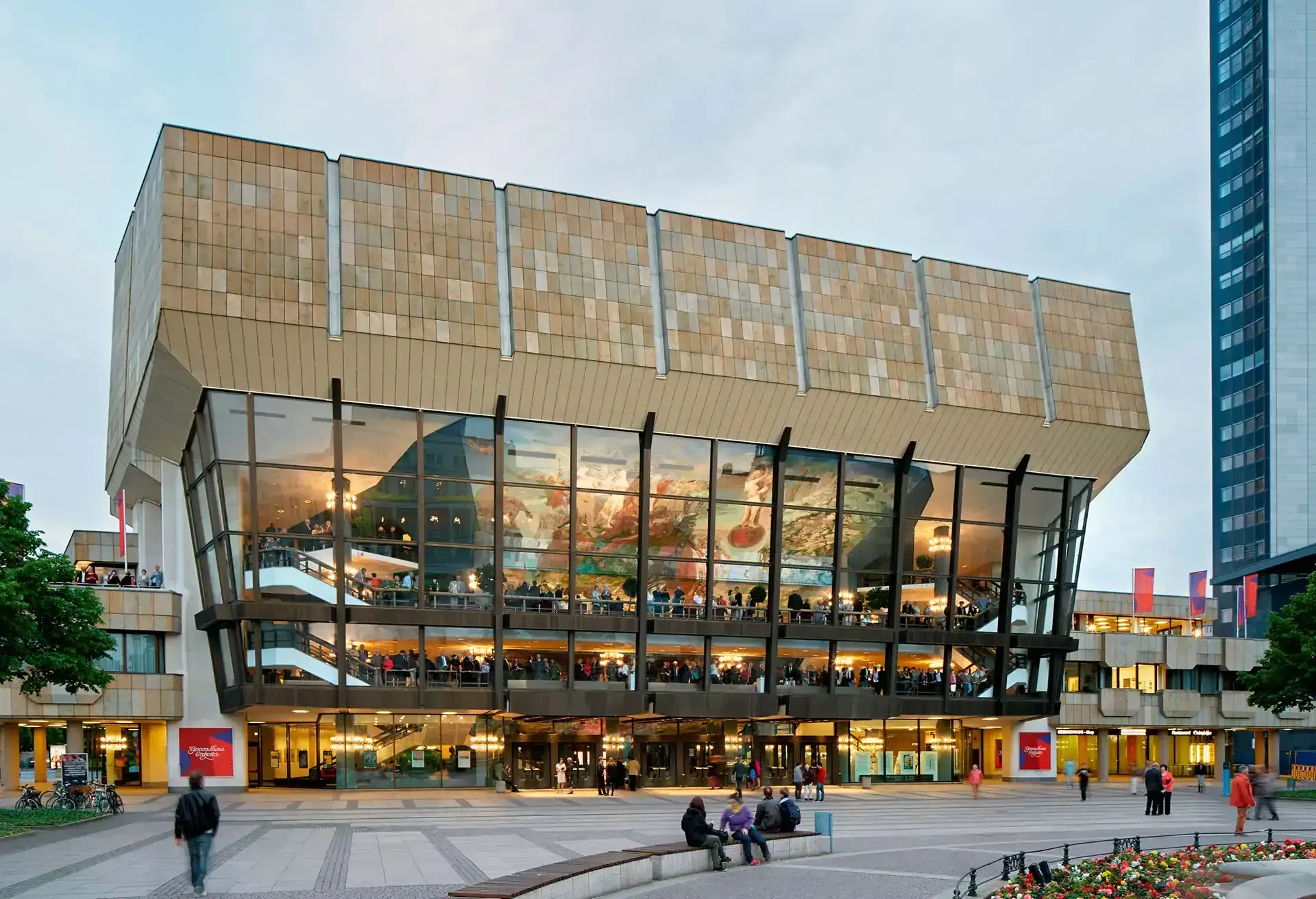 Moderne bygning med stor glasfacade og mennesker omkring på torvet.