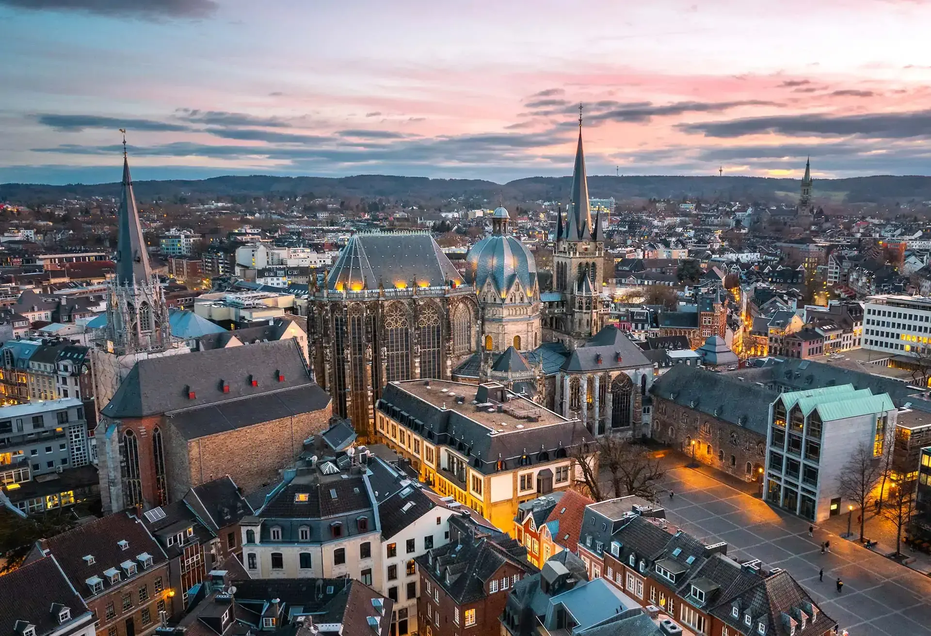 Panoramisk udsigt over Aachen by med historiske bygninger og kirker ved solnedgang.