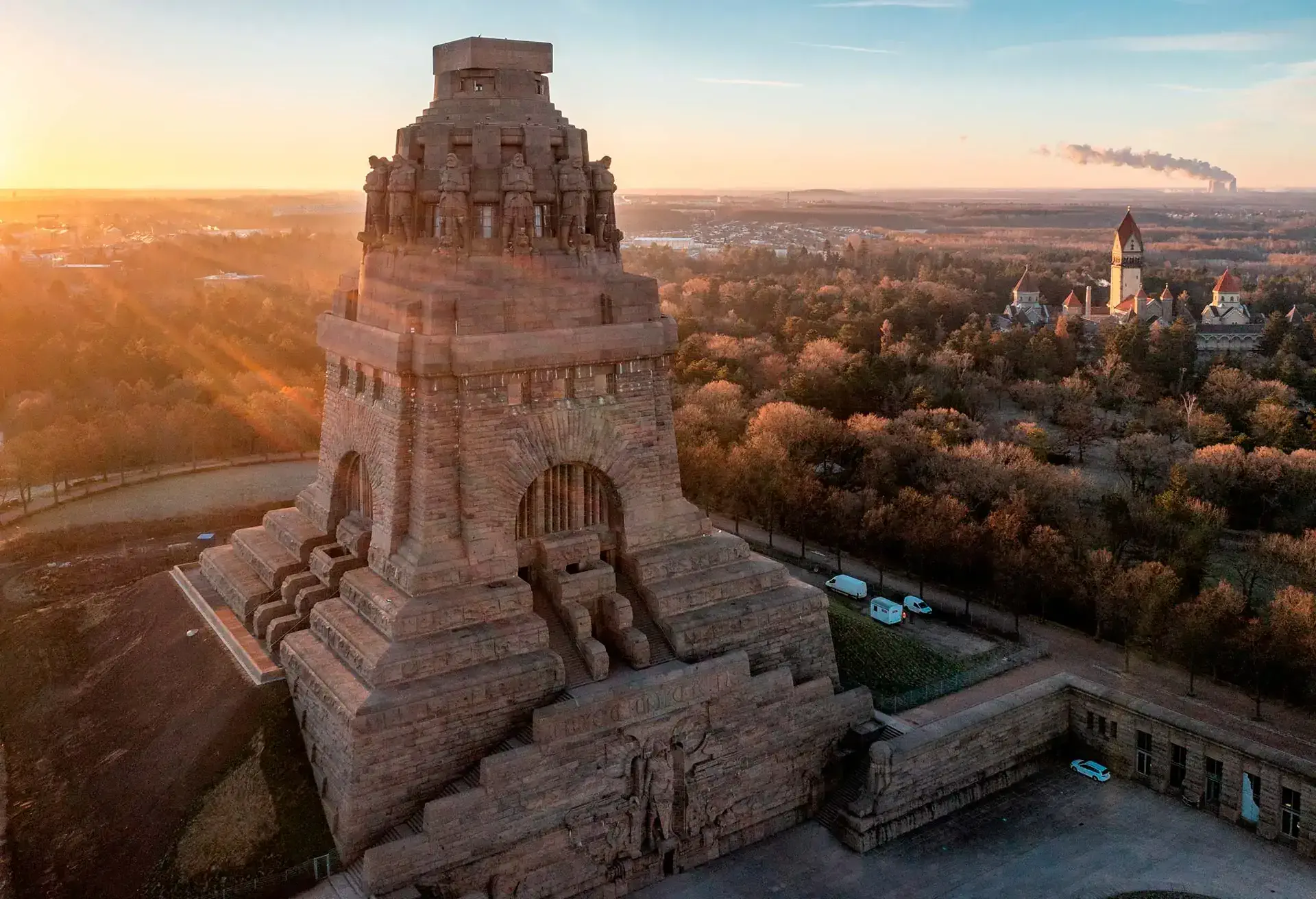 Storslået monument i solnedgangen med omgivelser af træer og bygninger i baggrunden.