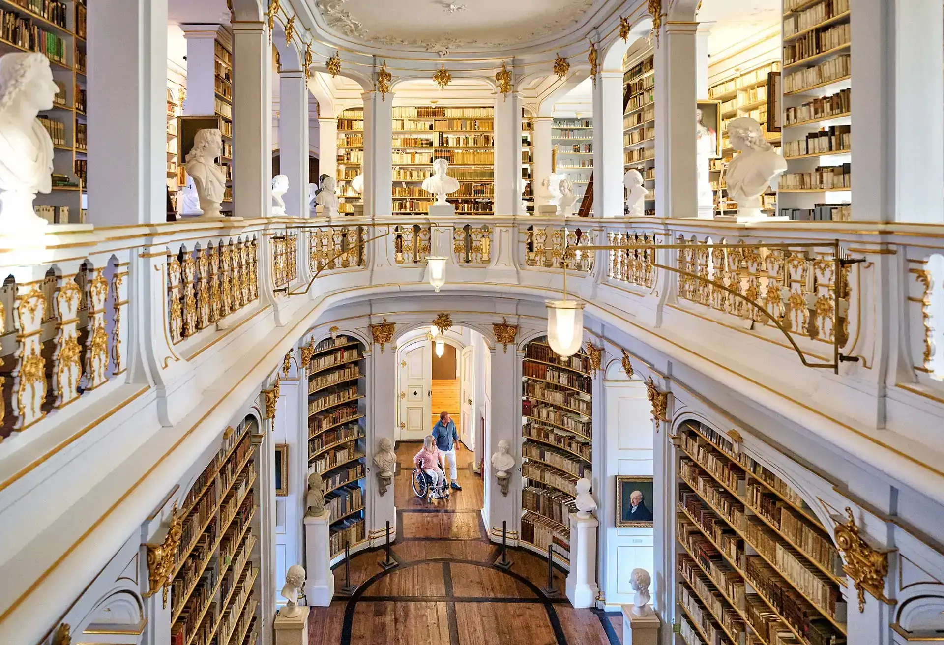 Historisk bibliotek med smukt indrettede hylder og statuer i en storslået sal.