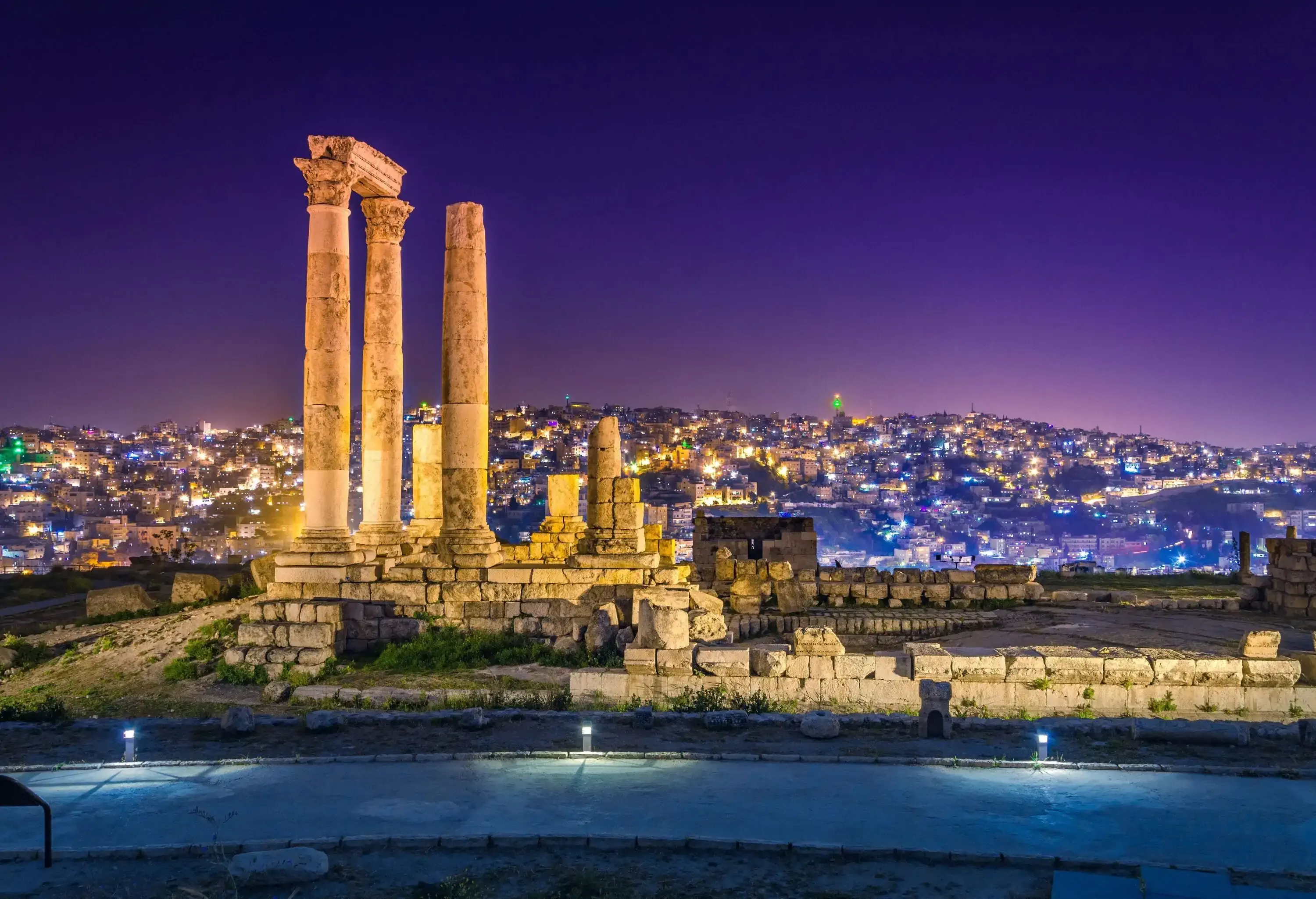 The Temple of Hercules in the Amman Citadel overlooking the illuminated cityscape.